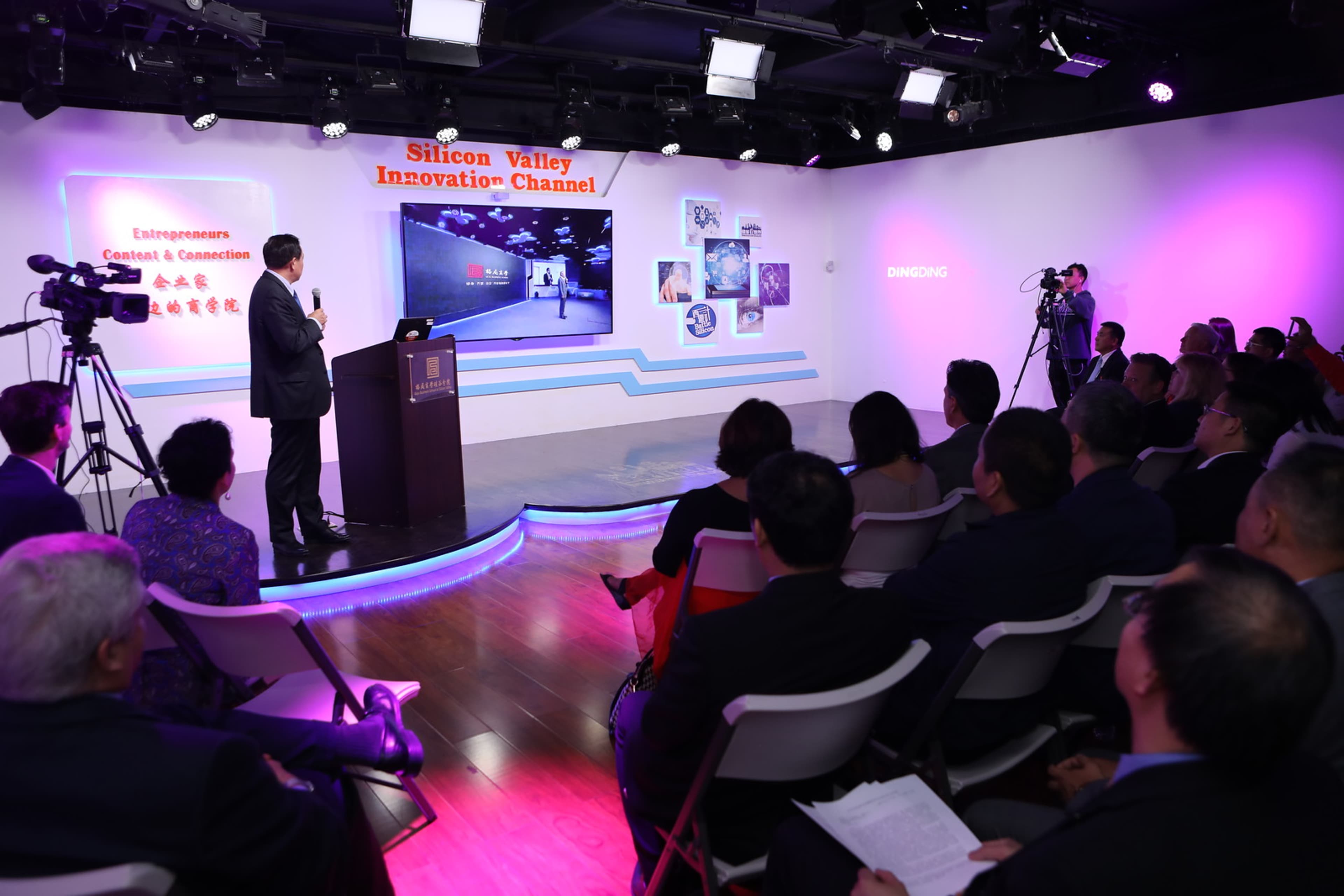 A speaker presents in front of an audience at the Silicon Valley Innovation Channel event, with cameras capturing the presentation on a screen.