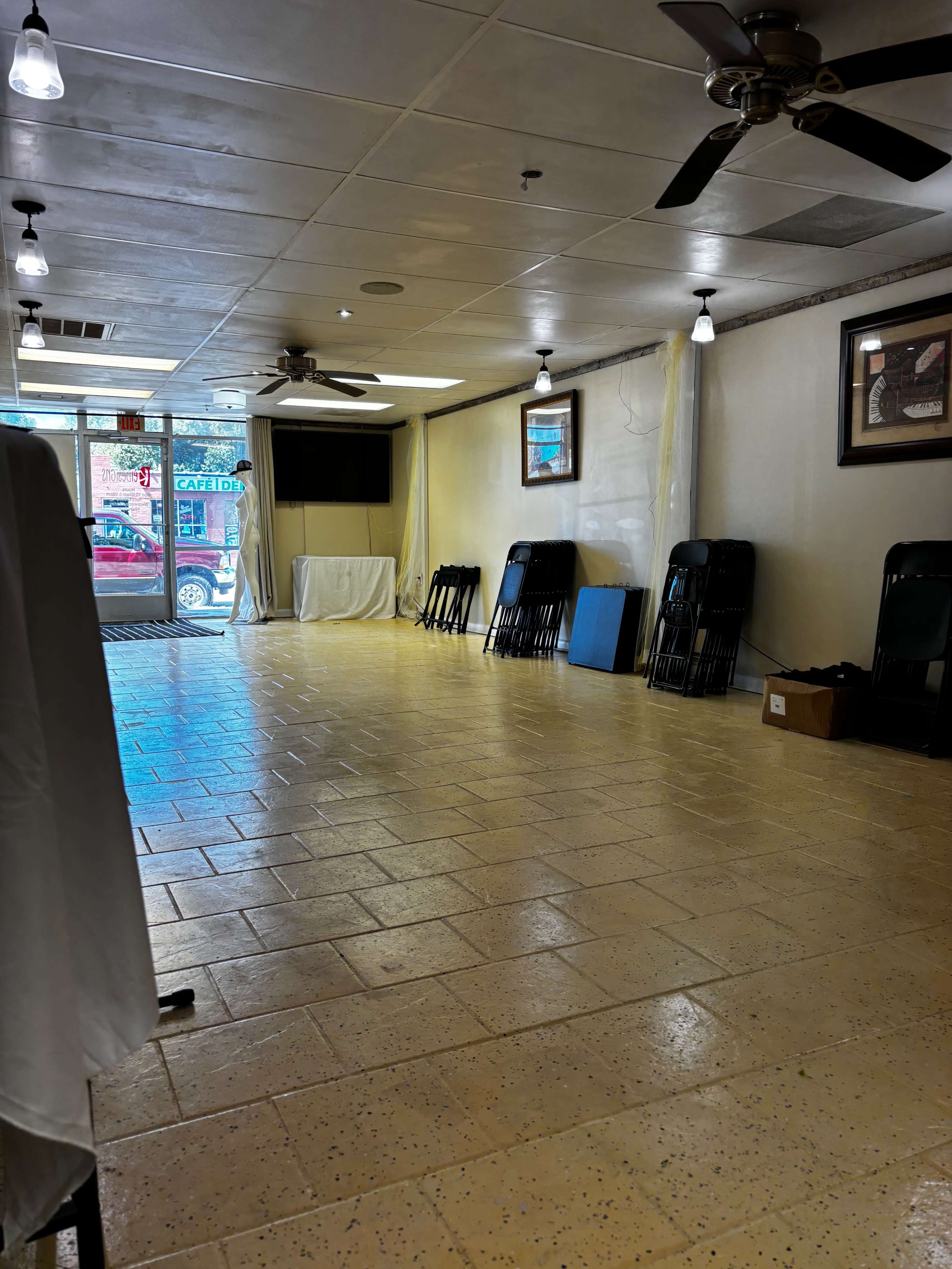 An empty indoor space with a tiled floor, several stacked chairs, and two ceiling fans.
