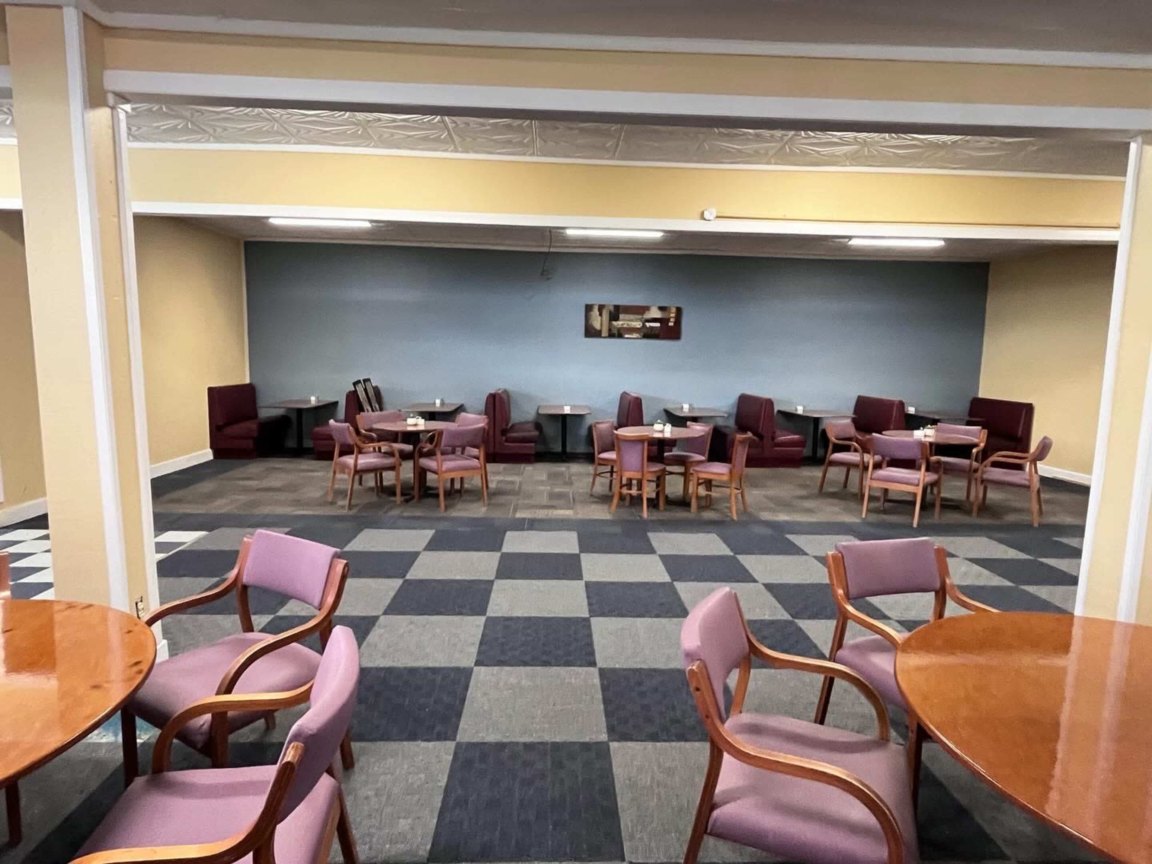 The image shows a spacious room with several round tables and chairs arranged in a grid pattern on a tiled floor.