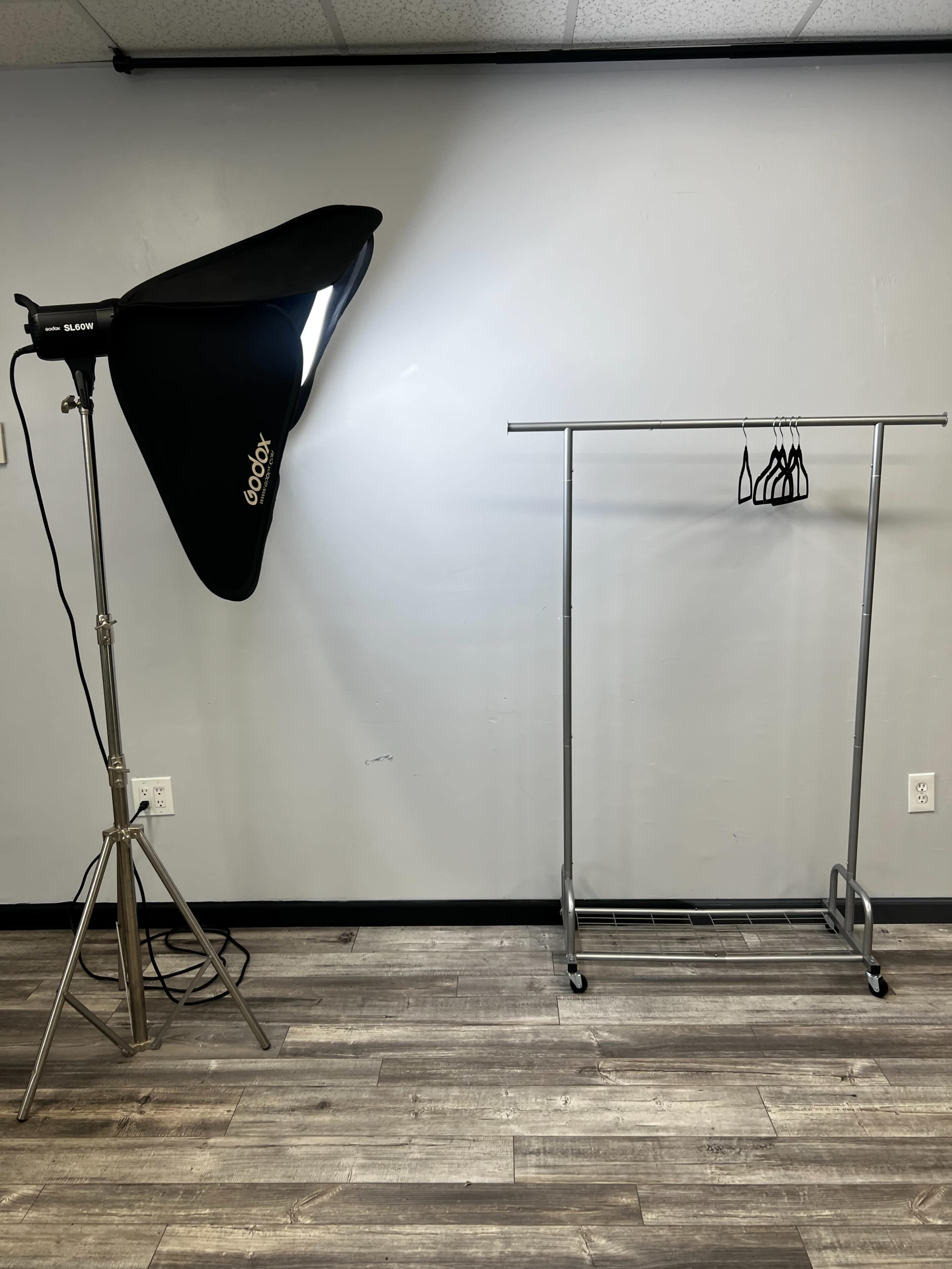 A photography setup features a light source on a stand next to a clothing rack with several hangers.