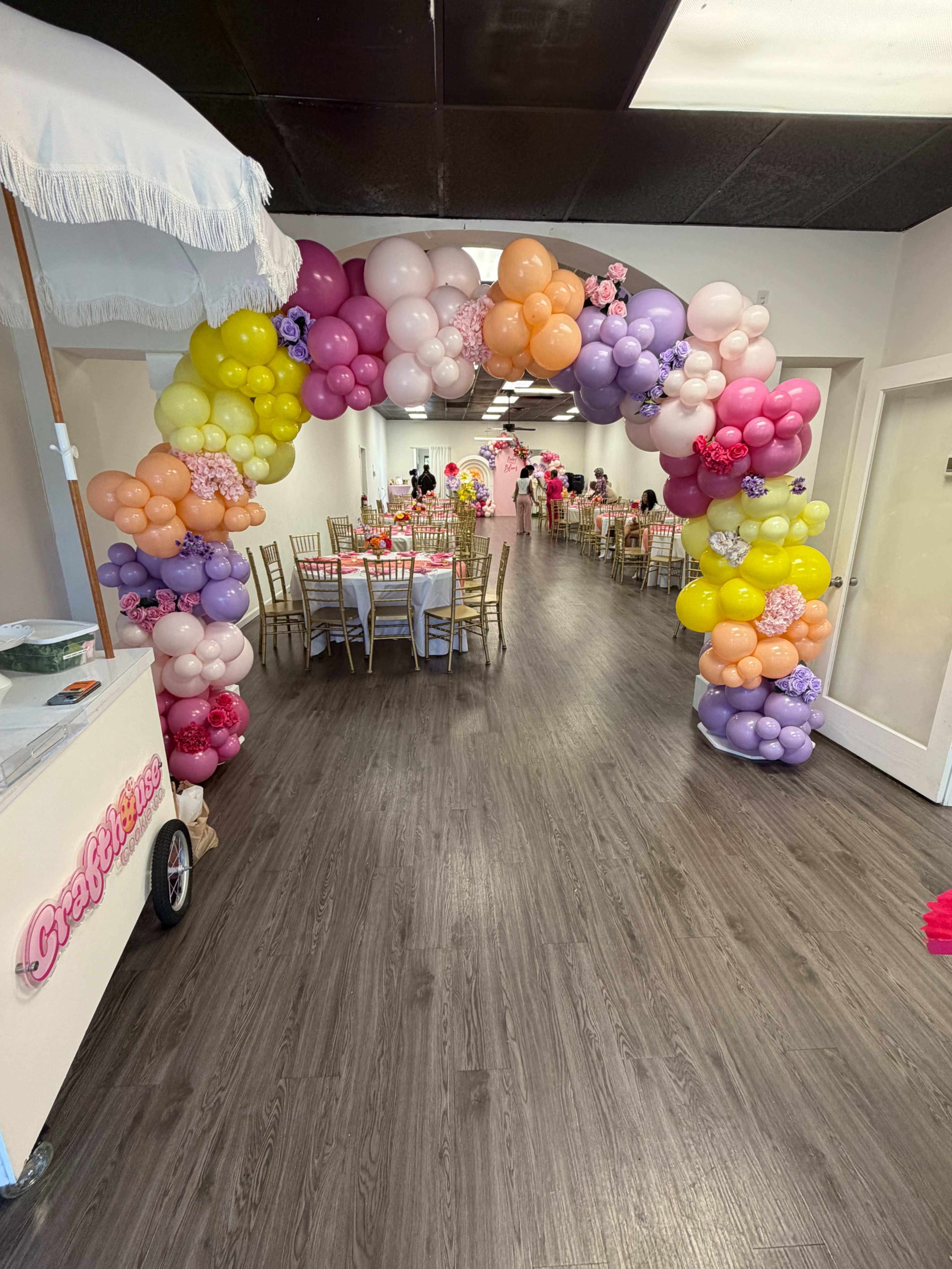 An arch made of colorful balloons frames a hallway leading to a decorated event space with tables set for a celebration.