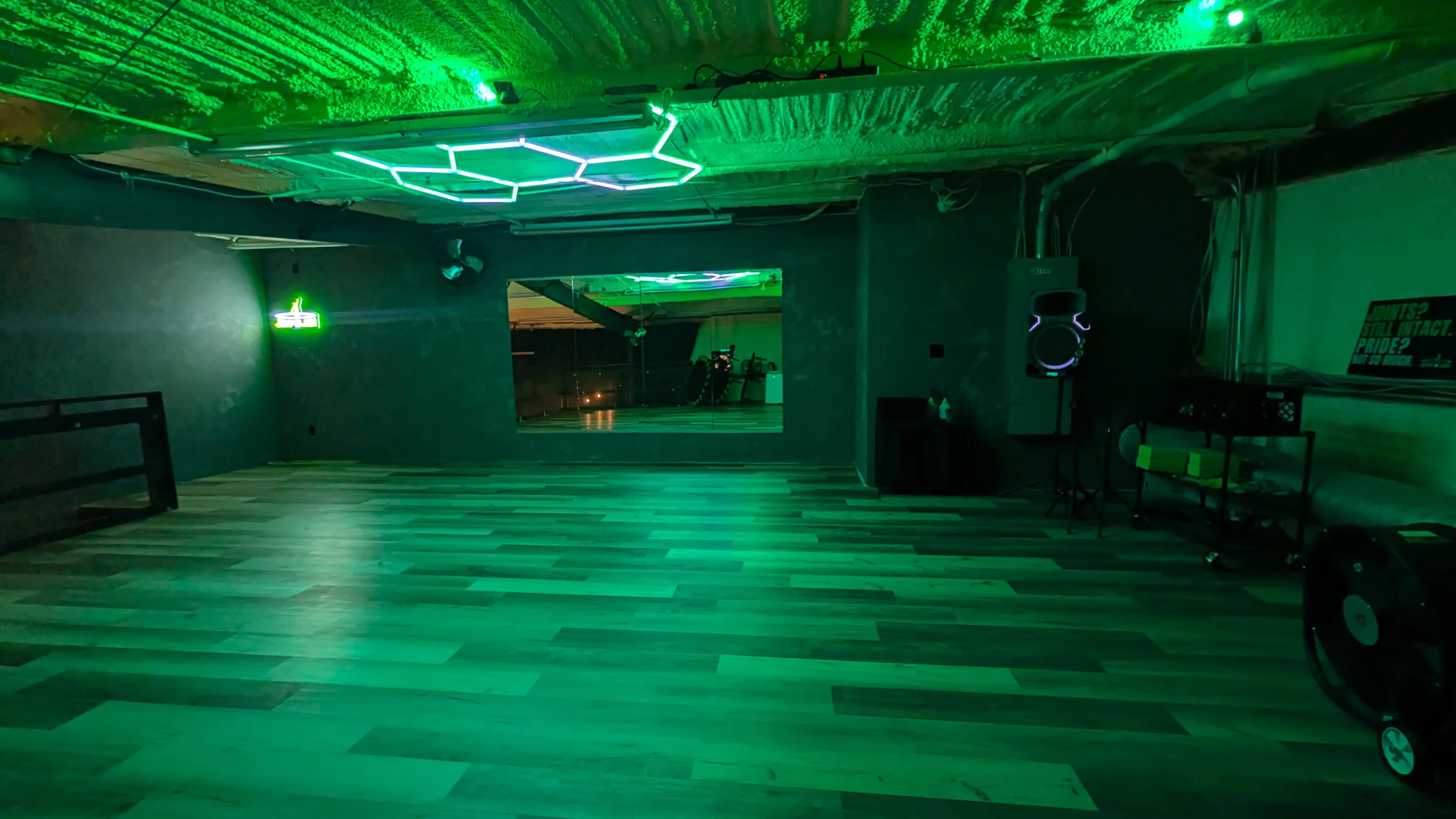 The image shows an empty room with green lighting, wood flooring, and a mirror reflecting part of the space.