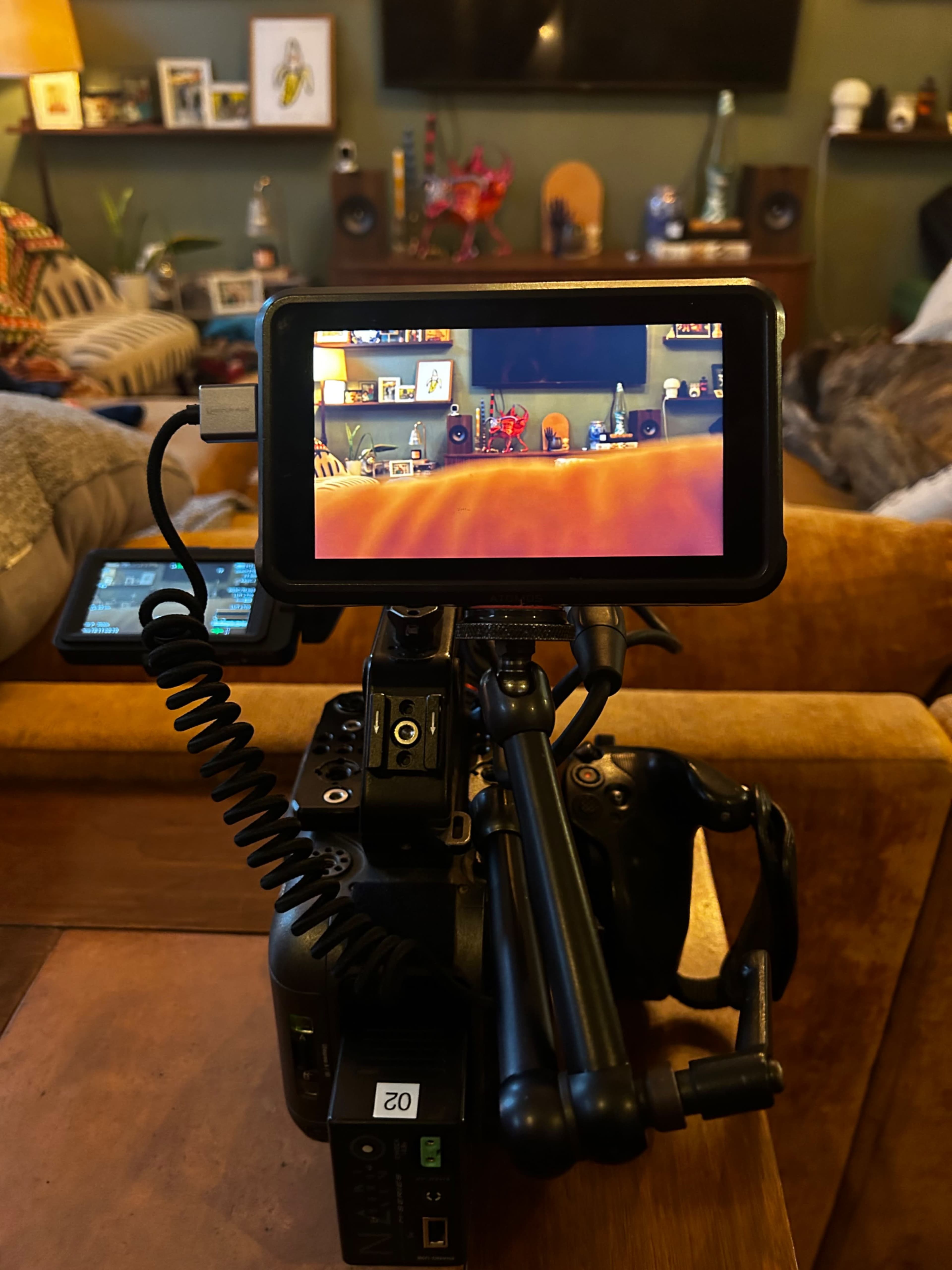 A camera sits on a table, displaying a colorful gaming scene on its monitor while a cozy living room is visible in the background.
