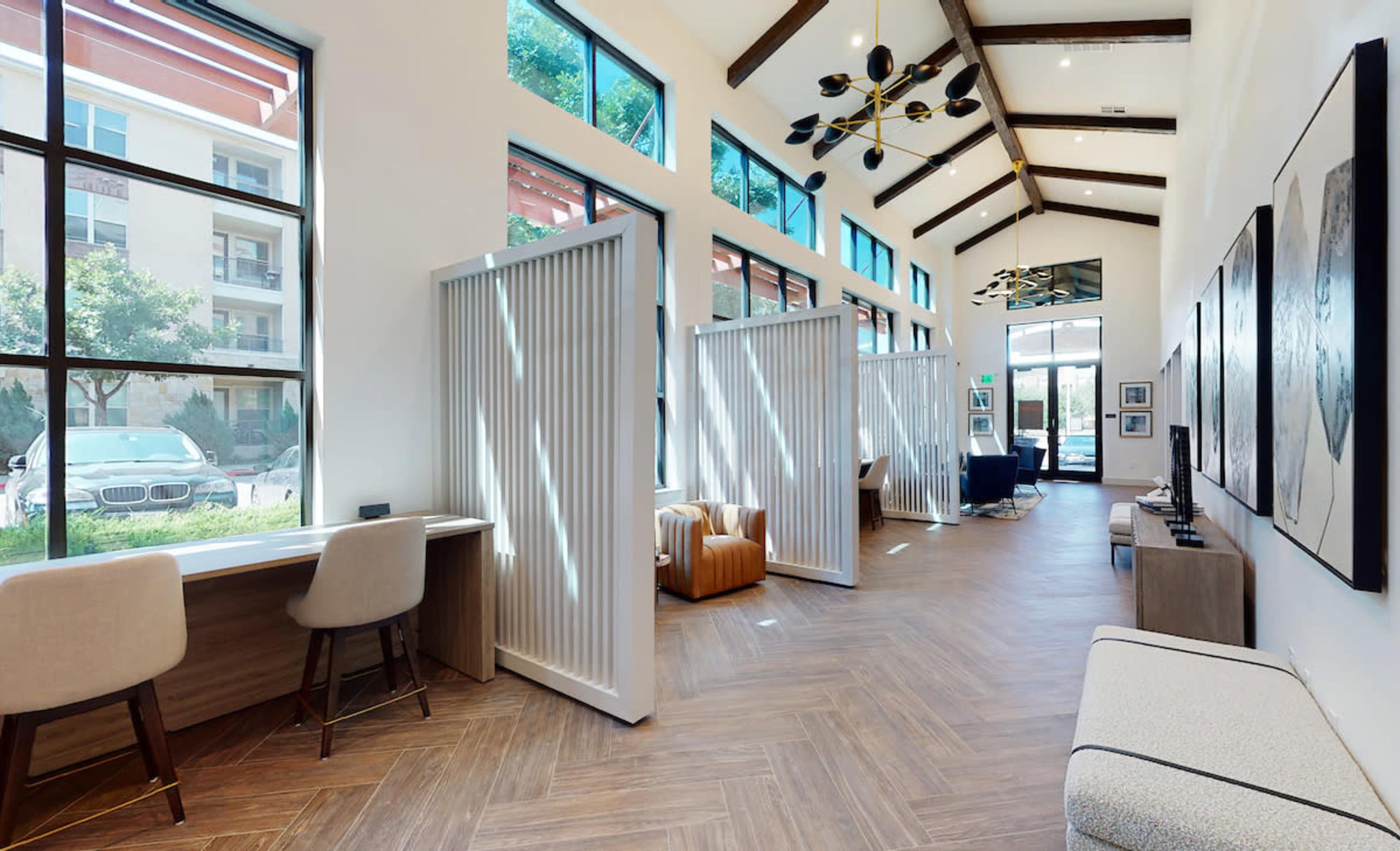 A spacious interior designed as a modern lounge area with tall windows, wooden beams, and partitioned seating spaces.