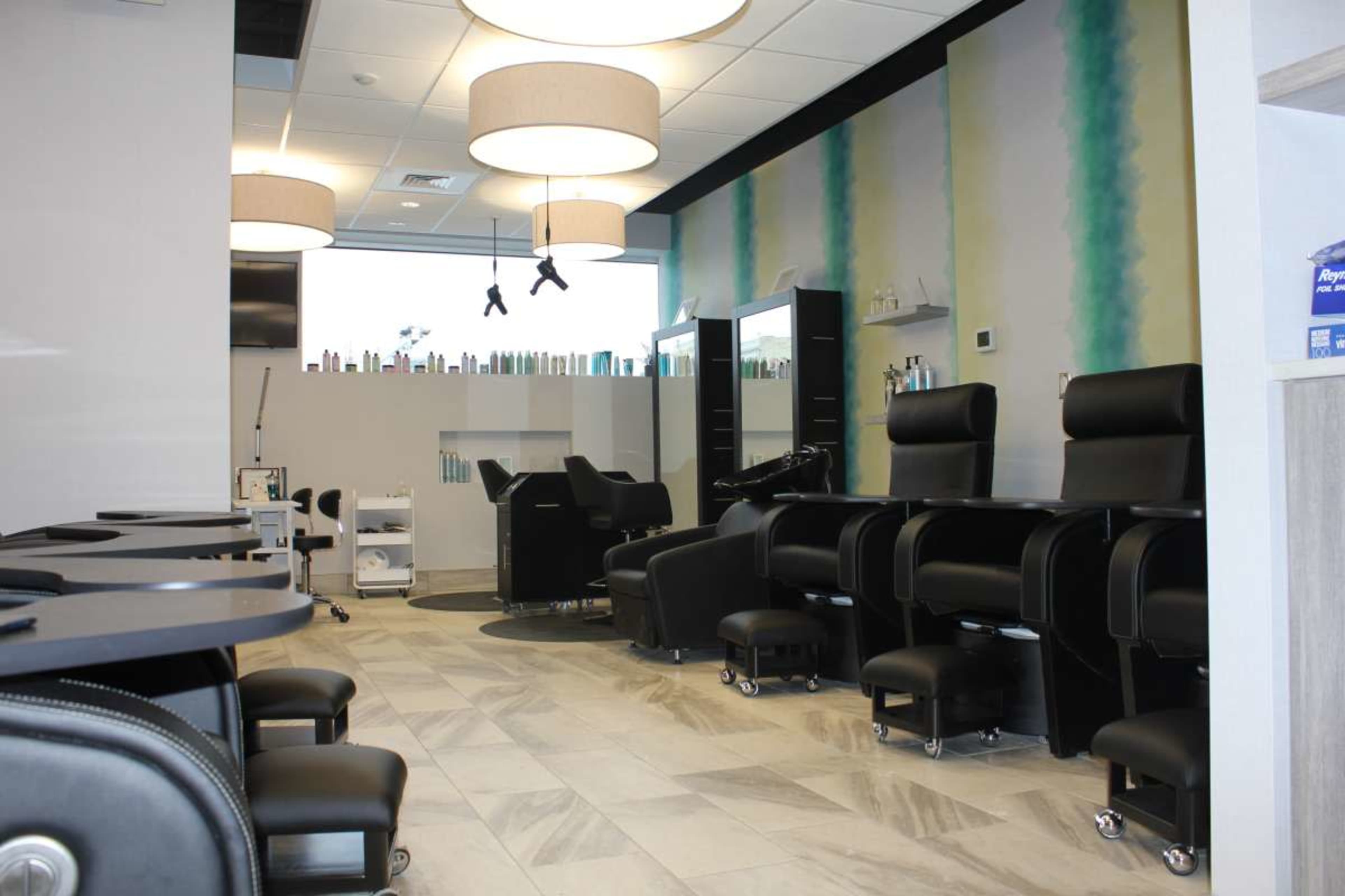 The image depicts a modern salon interior with black styling chairs, mirrors, and shelves of hair care products in a well-lit environment.