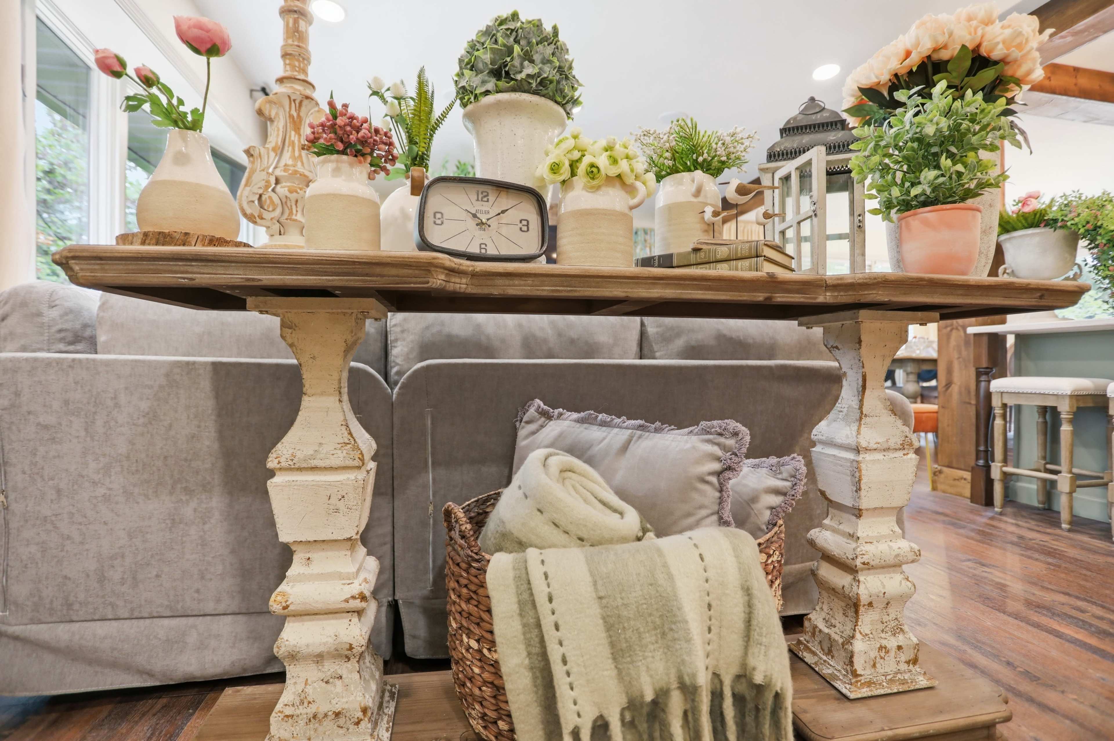 A wooden table with decorative vases and a clock sits in front of a gray couch in a cozy living space.