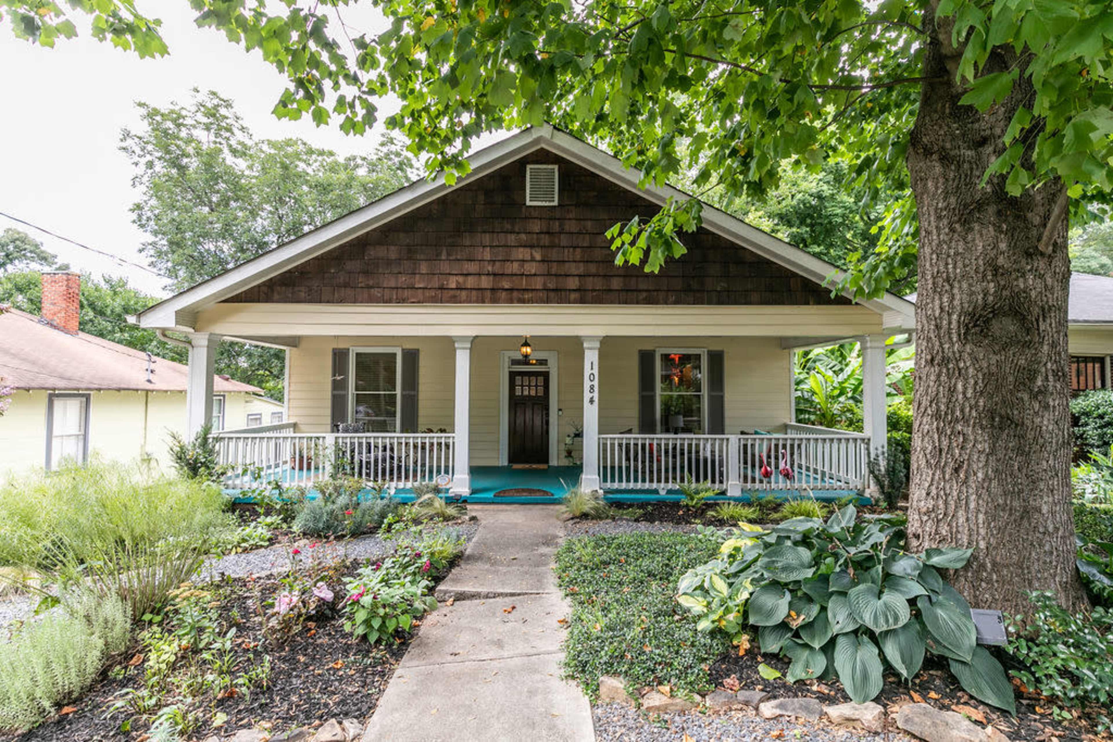 A single-story house with a front porch, surrounded by a garden featuring various plants and flowers.
