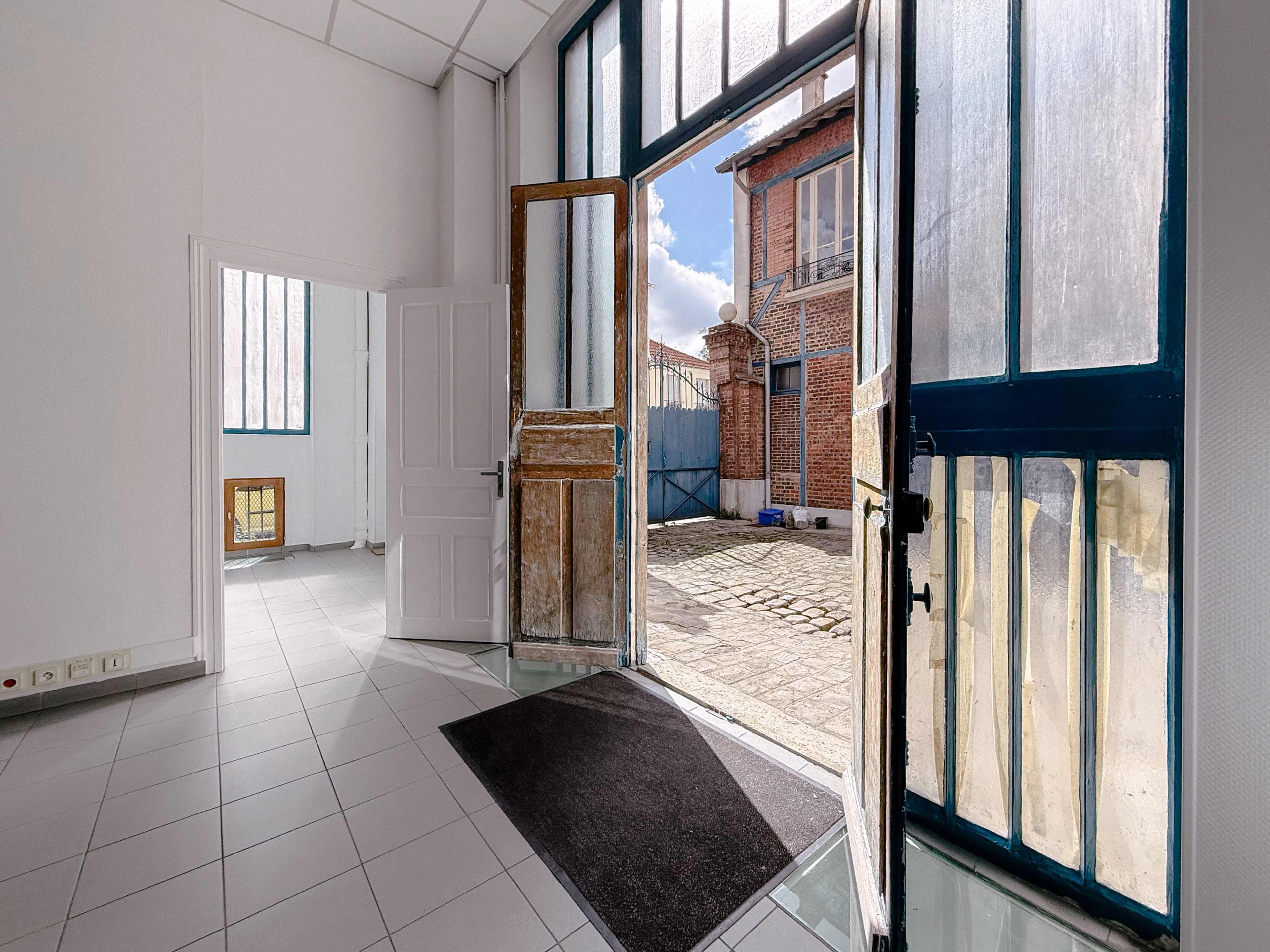 The image shows an entrance area with a partially open double door leading to a well-lit outdoor space.