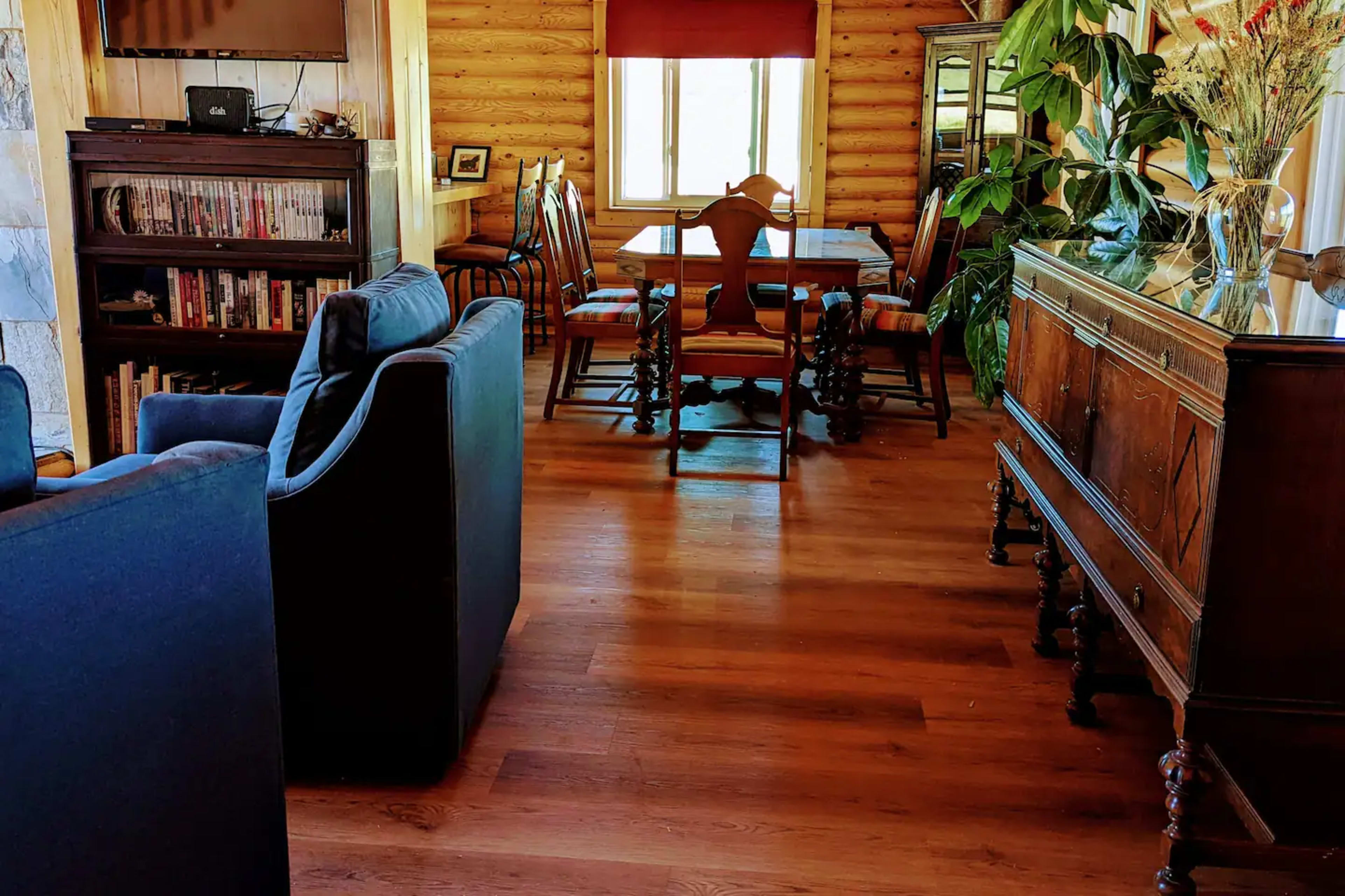 A cozy room with wooden walls, a dining table surrounded by chairs, and a living area featuring blue sofas and a wooden sideboard.