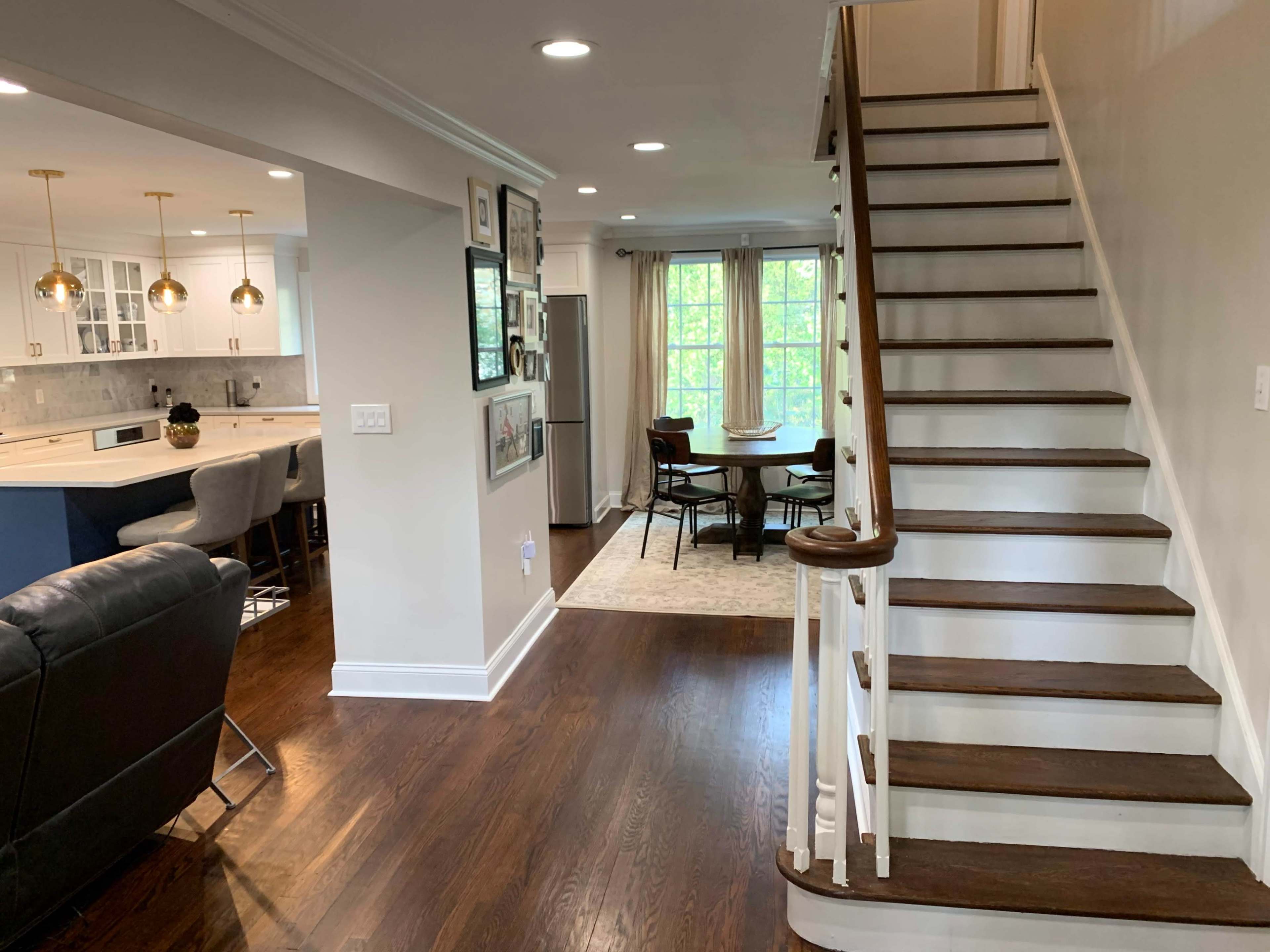 A well-lit interior hallway leading to a staircase, with a dining area visible at the end and a kitchen to the left.