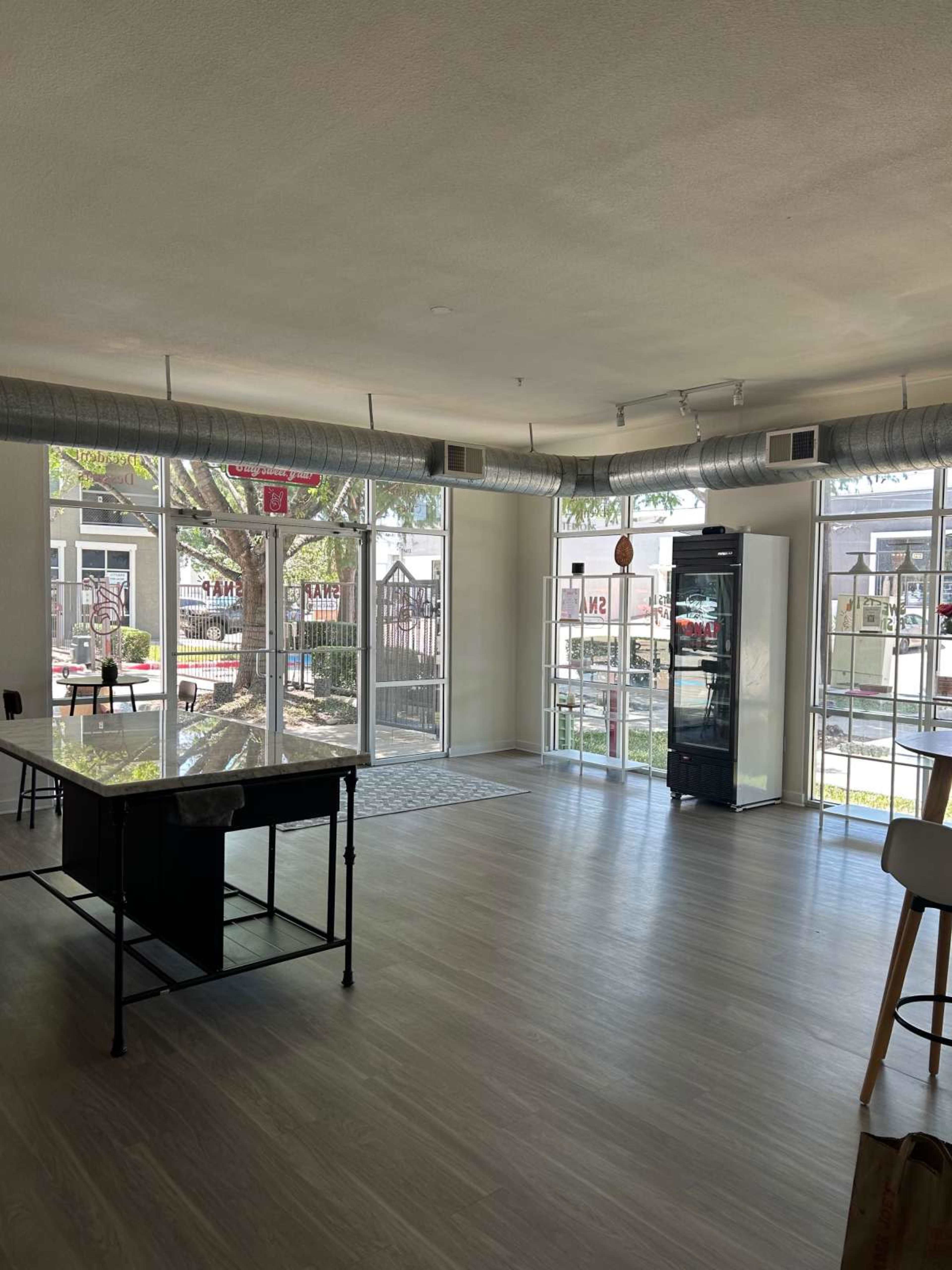 The image shows an empty, well-lit room with large windows, a marble-topped table, and a glass-front refrigerator.