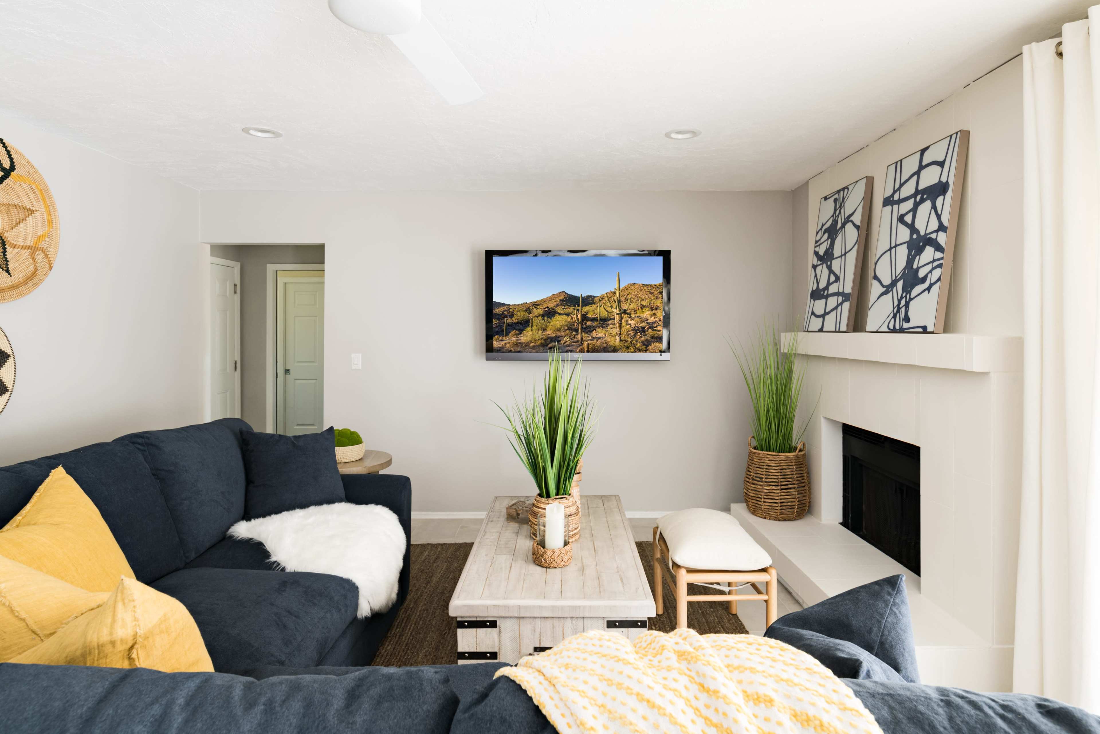 A modern living room features a dark sofa, a wooden coffee table, and a mounted television displaying a desert landscape.