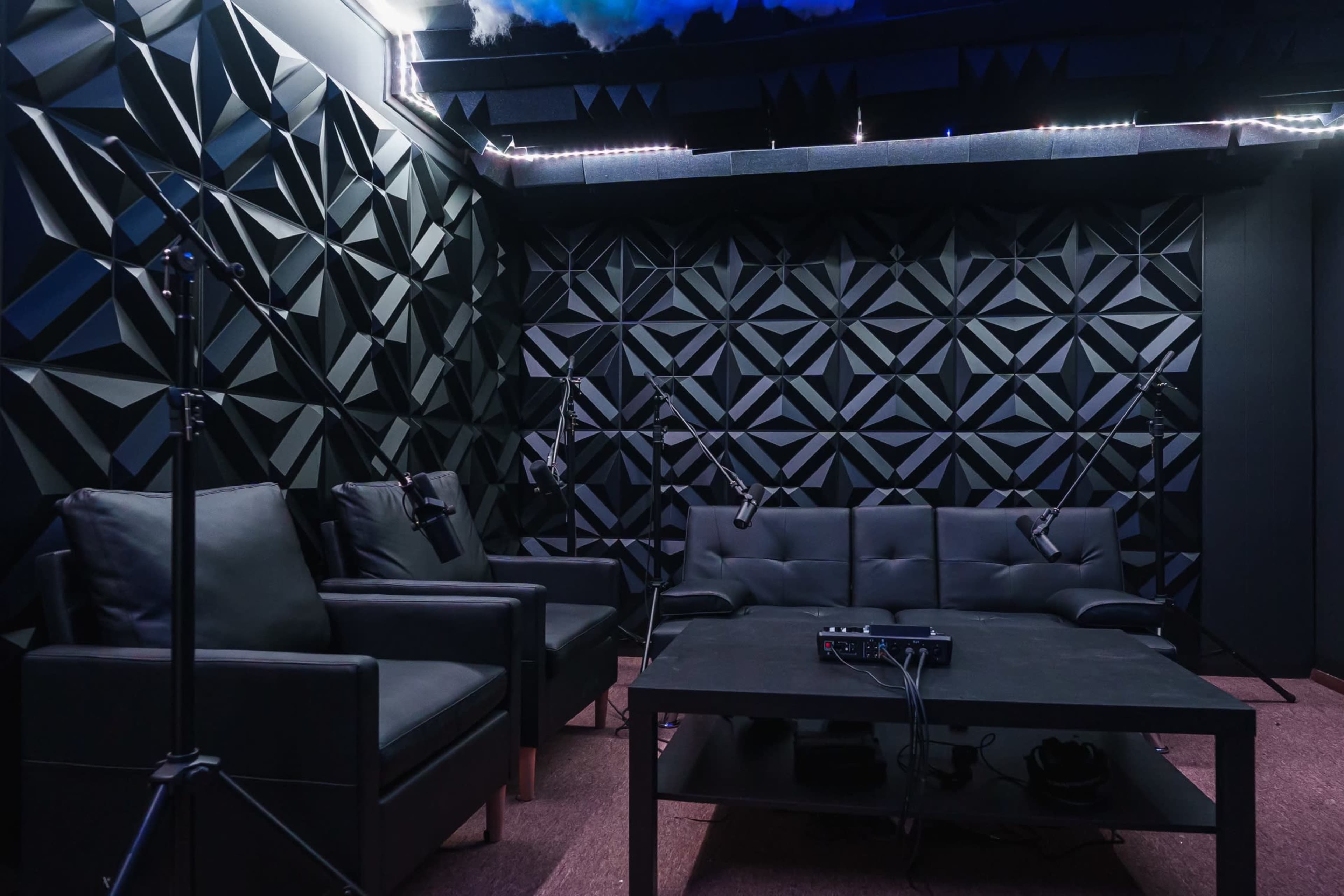 A soundproof recording studio with black geometric-patterned walls, a black sofa, and multiple microphones set up on stands.
