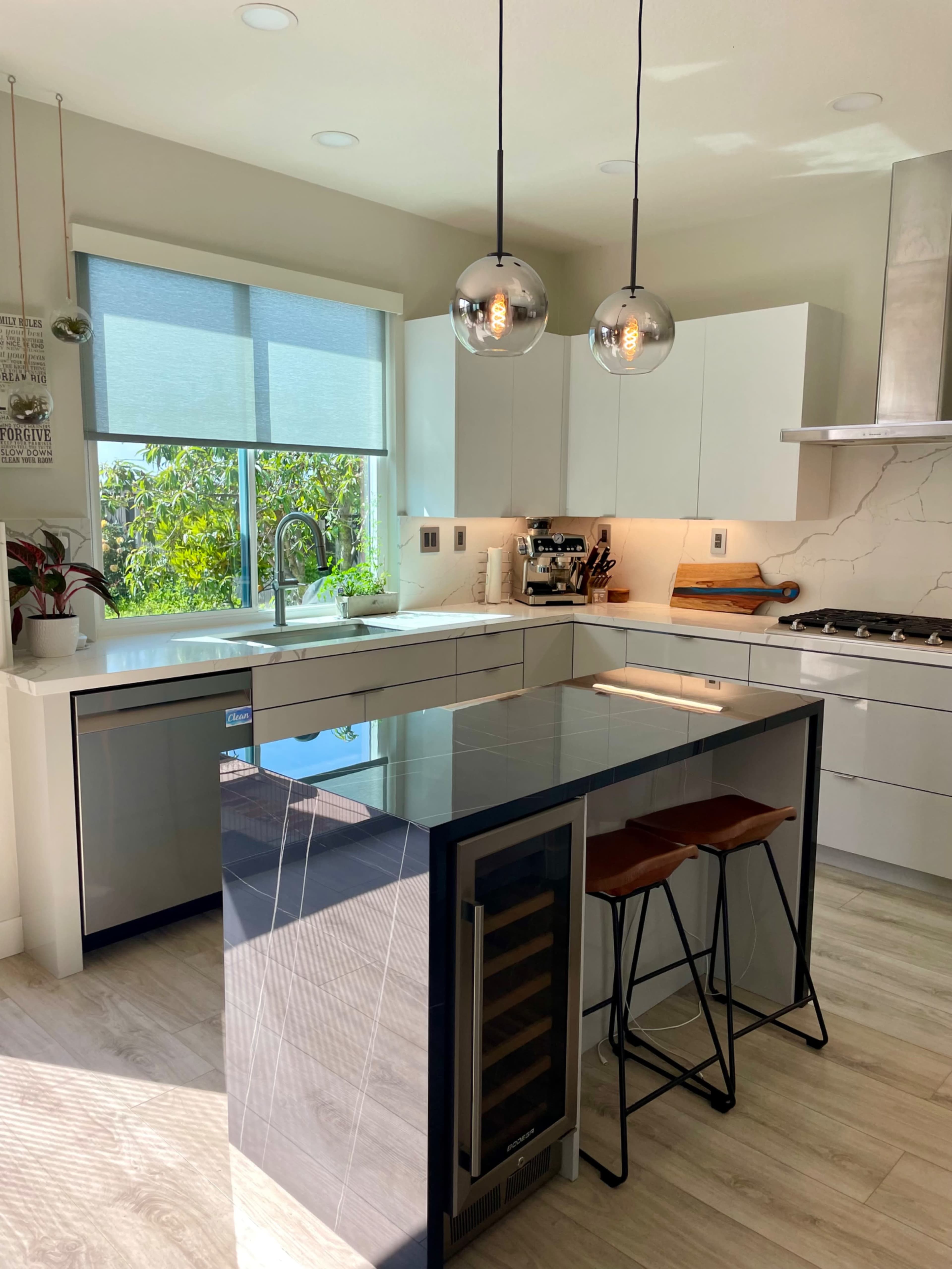 A modern kitchen with white cabinetry, an island featuring a dark countertop, and pendant lights hanging above.