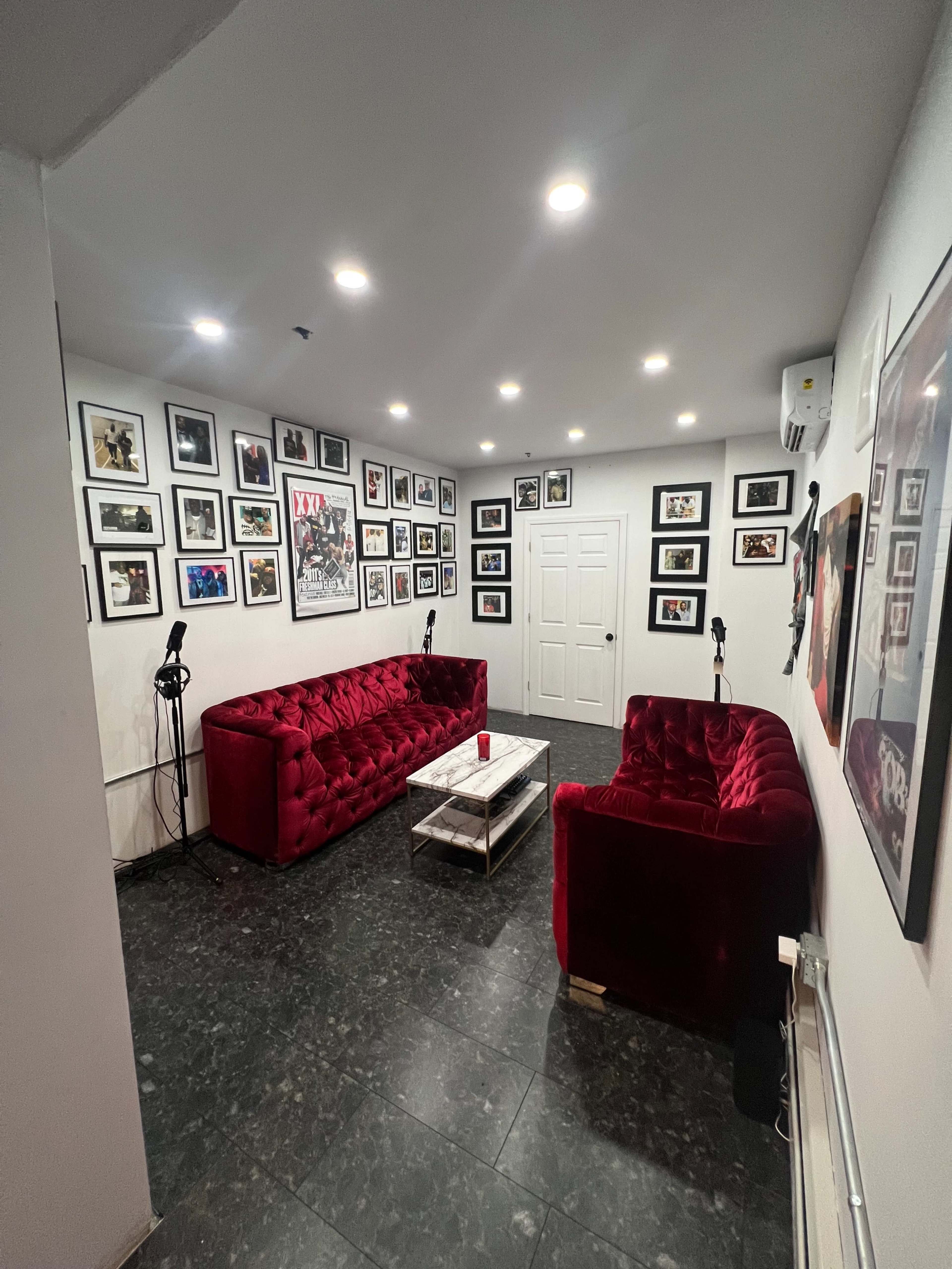The scene shows a small room with two red velvet sofas, a coffee table, and walls covered with framed photographs and art.