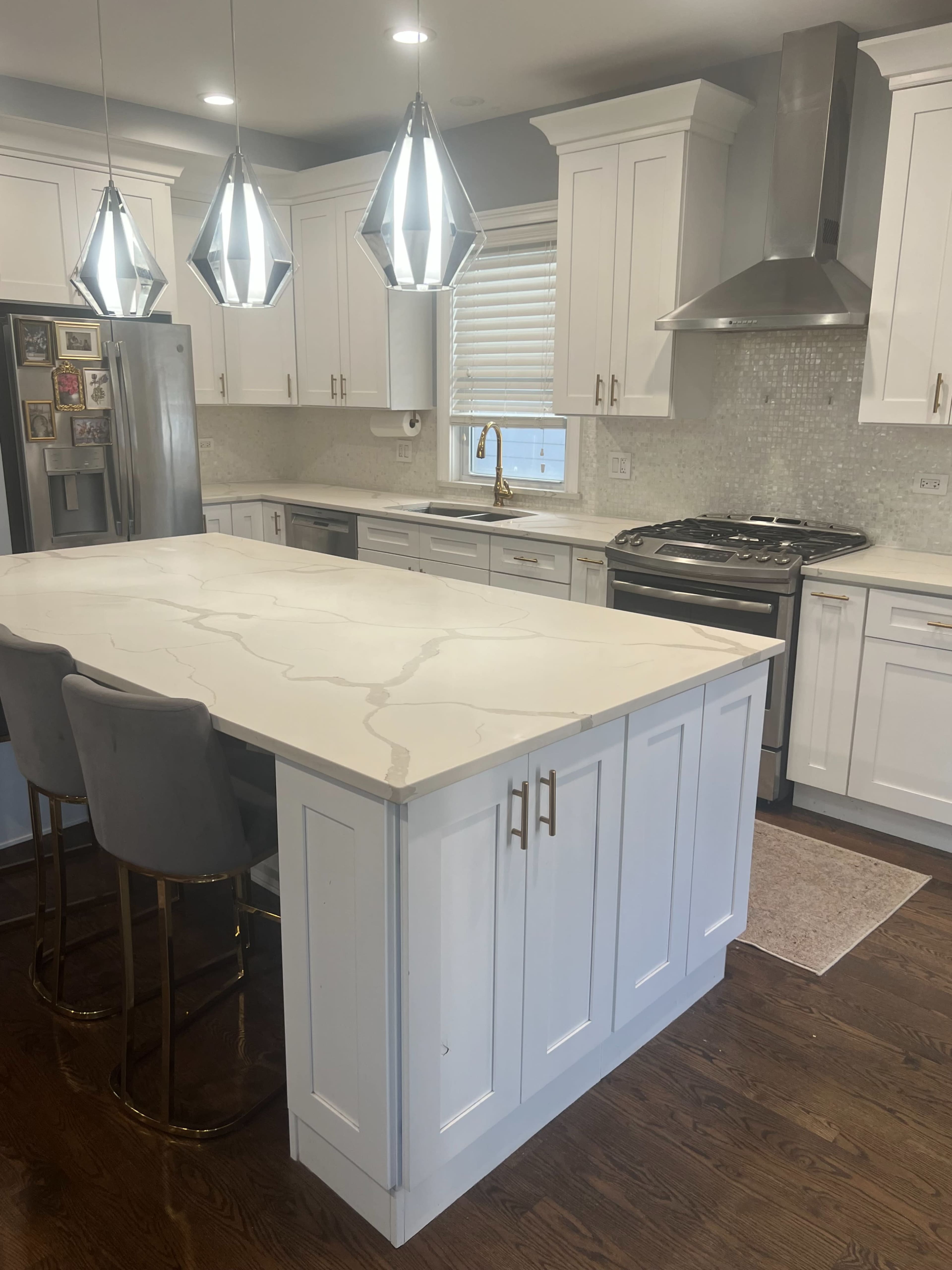The image shows a modern kitchen featuring white cabinetry, a large island with a marble countertop, and pendant lighting.