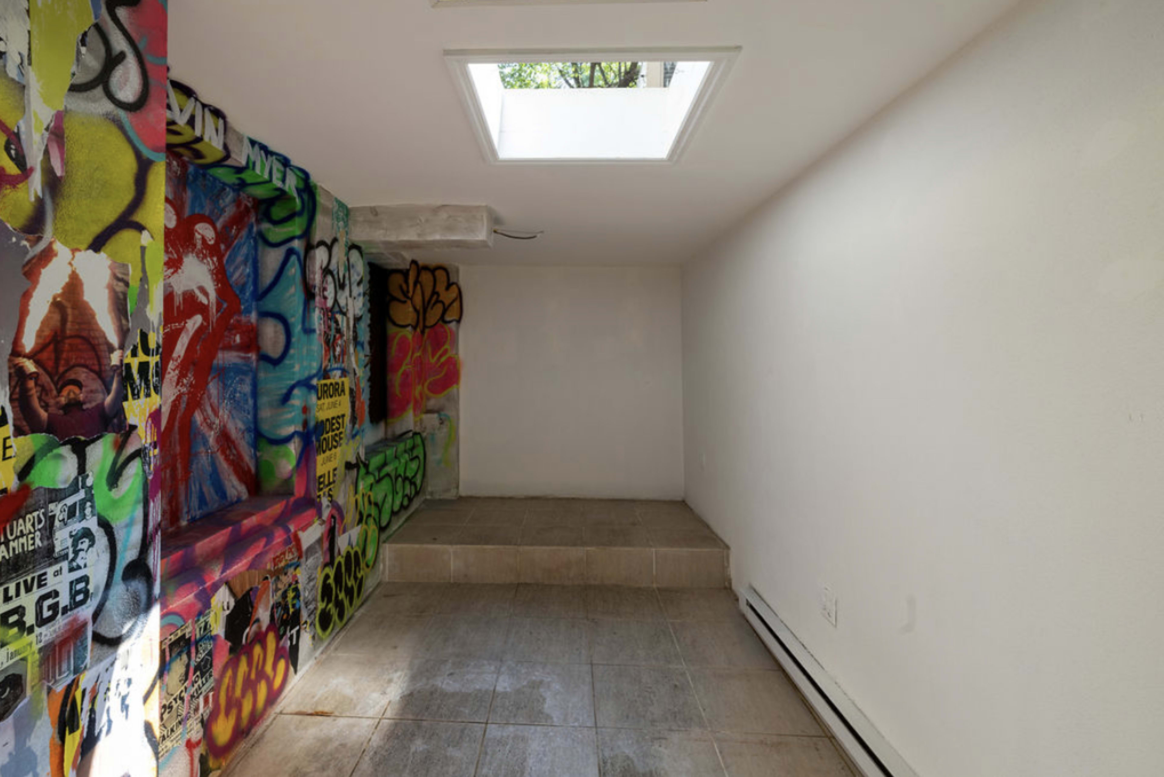 A small, partially finished room with a skylight and walls covered in colorful graffiti.