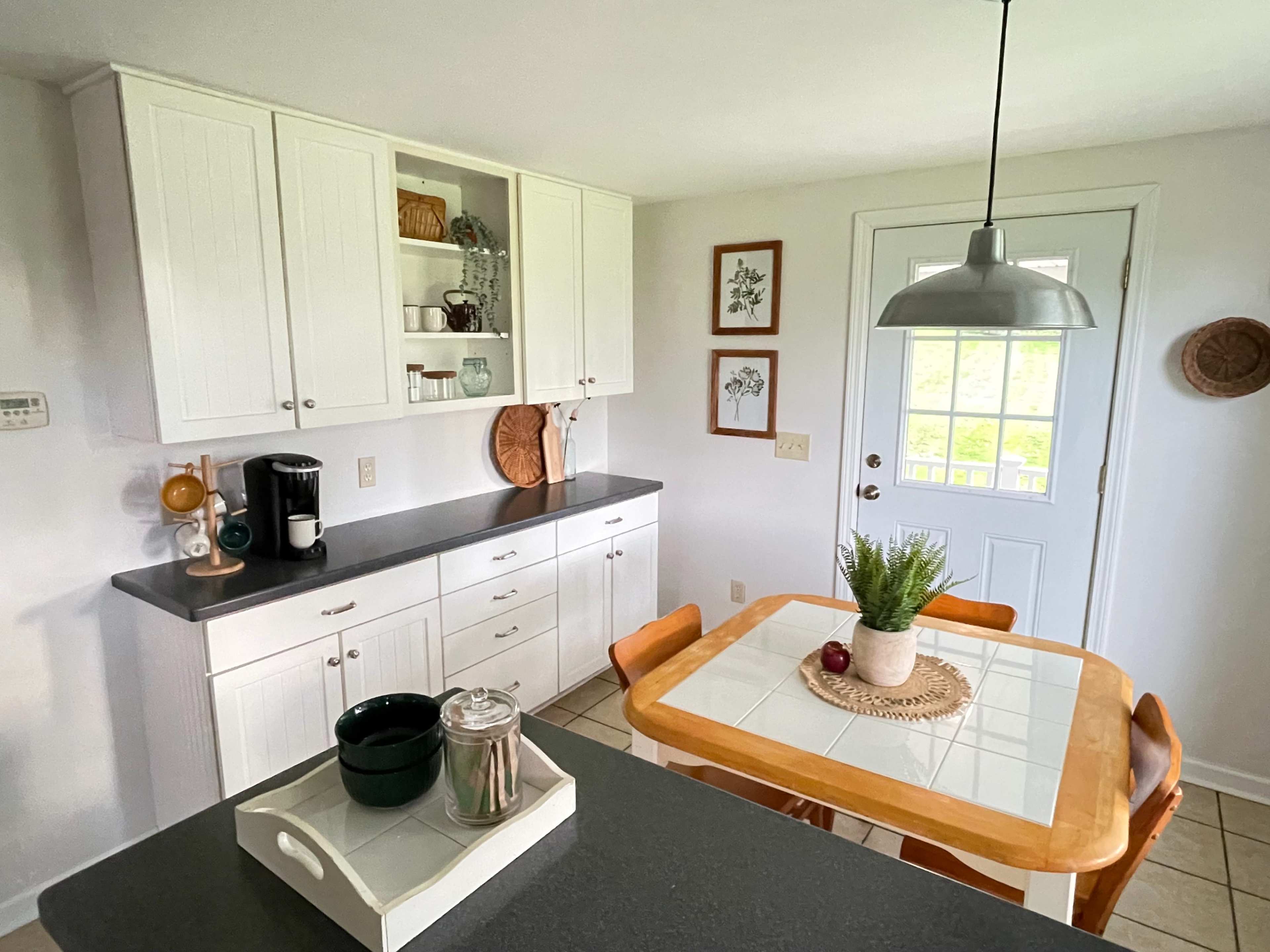 A bright kitchen with white cabinetry, a wooden table set for dining, and a door leading outside.
