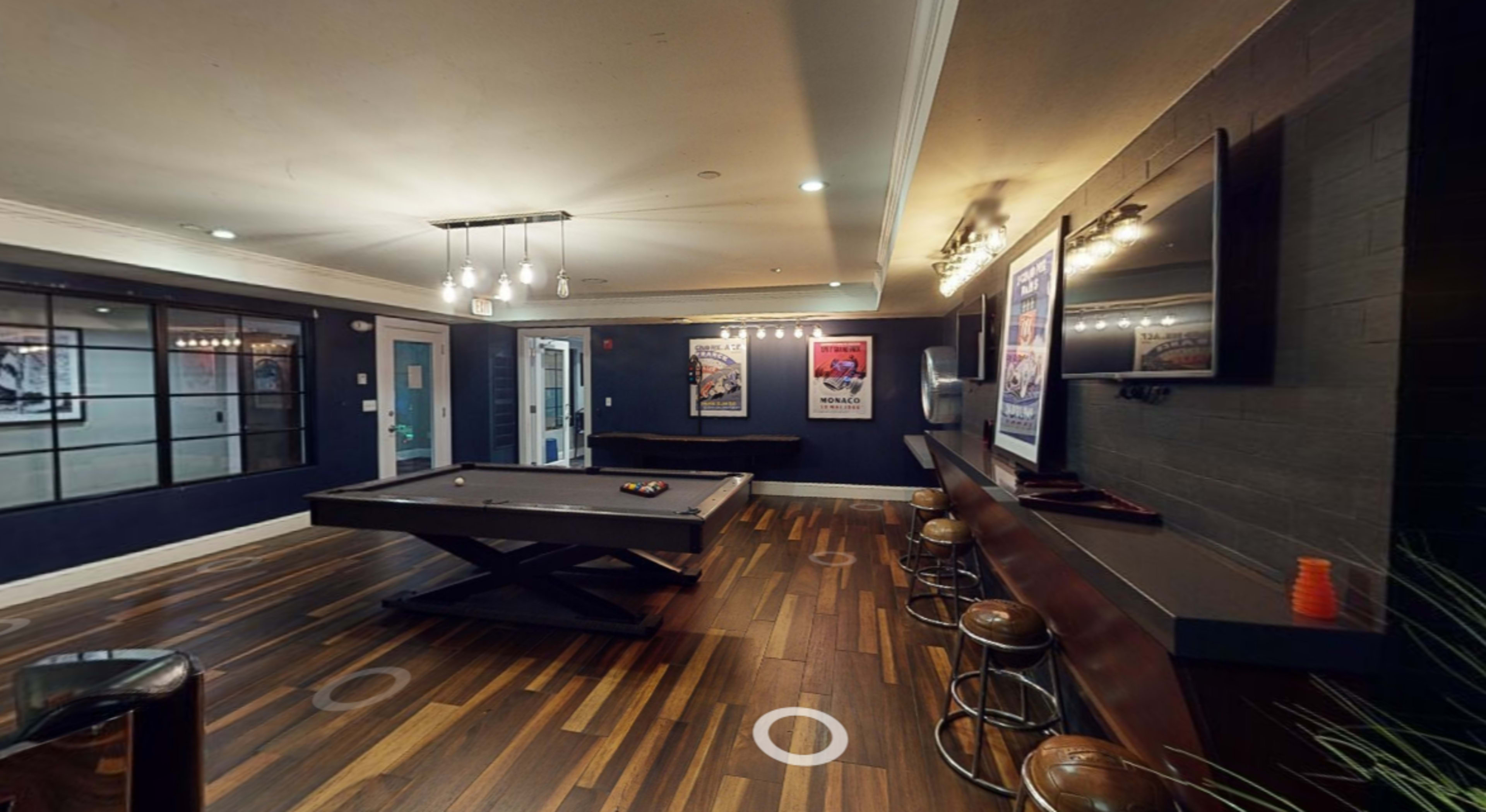 A game room with a pool table, bar seating, and framed posters on the walls.