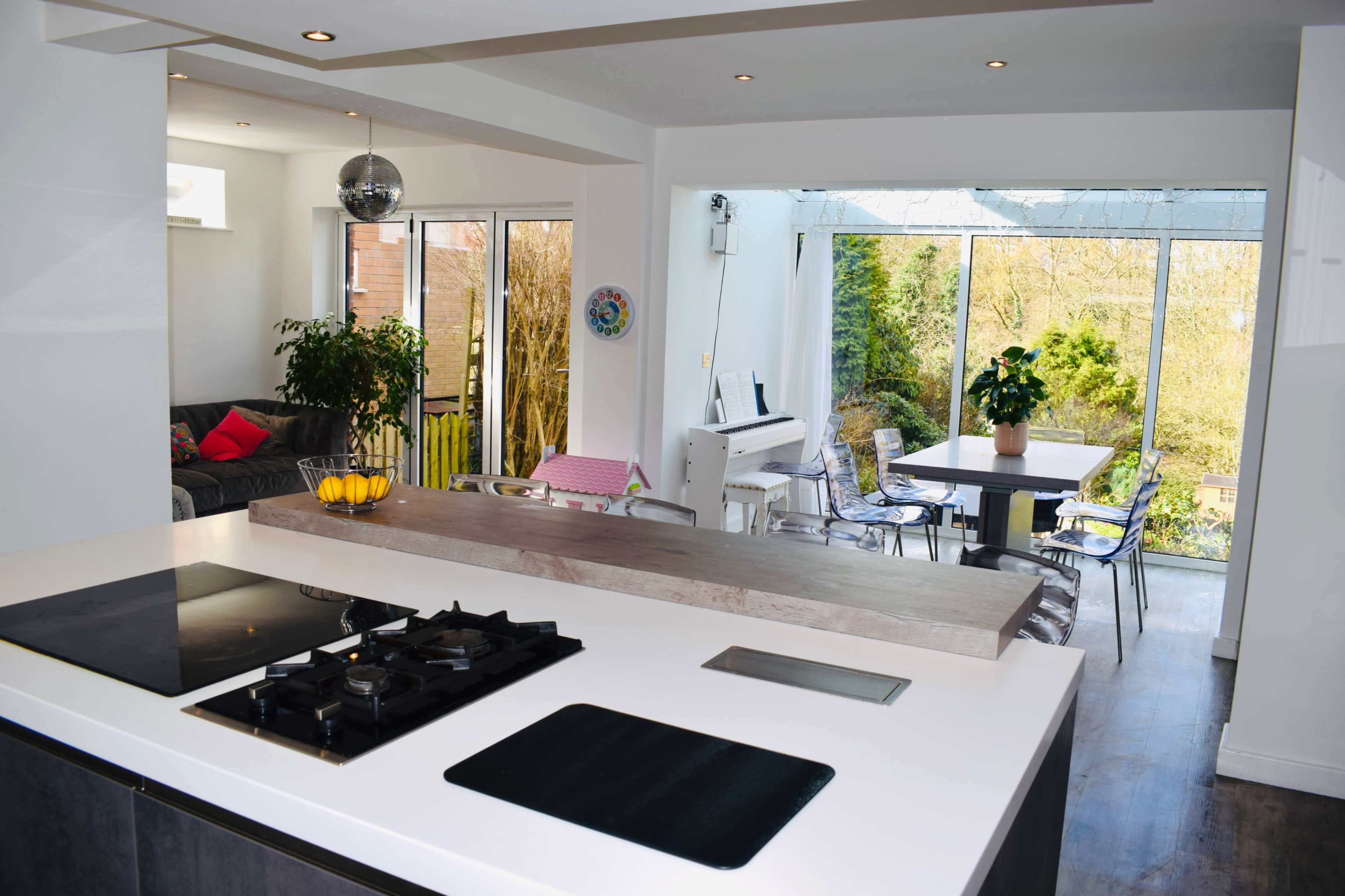 A modern kitchen with a gas stove and an island, adjacent to a dining area featuring a glass-enclosed patio overlooking a garden.