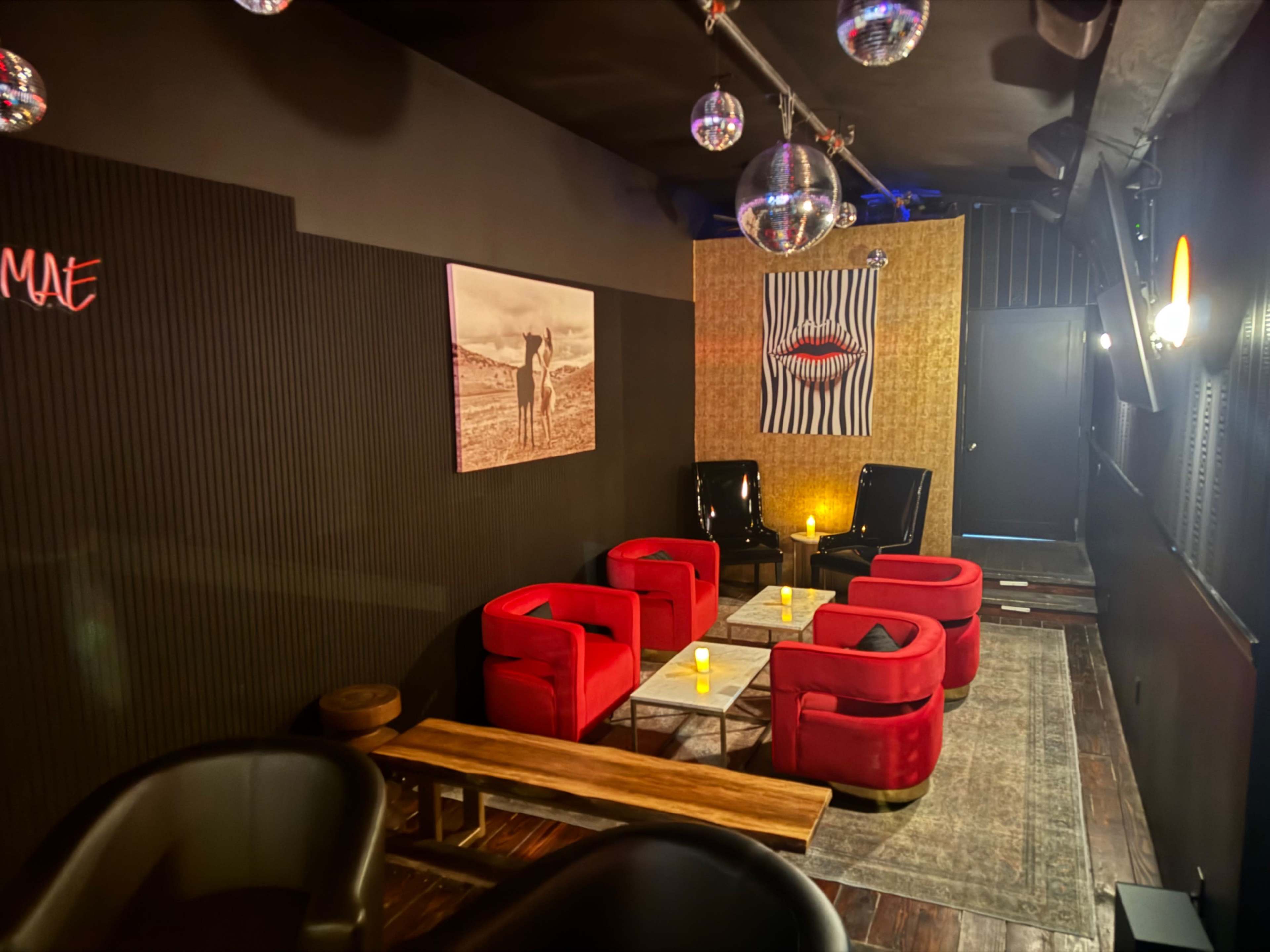 The image shows a dimly lit lounge area with red chairs arranged around a coffee table, featuring disco balls hanging from the ceiling and artwork on the walls.