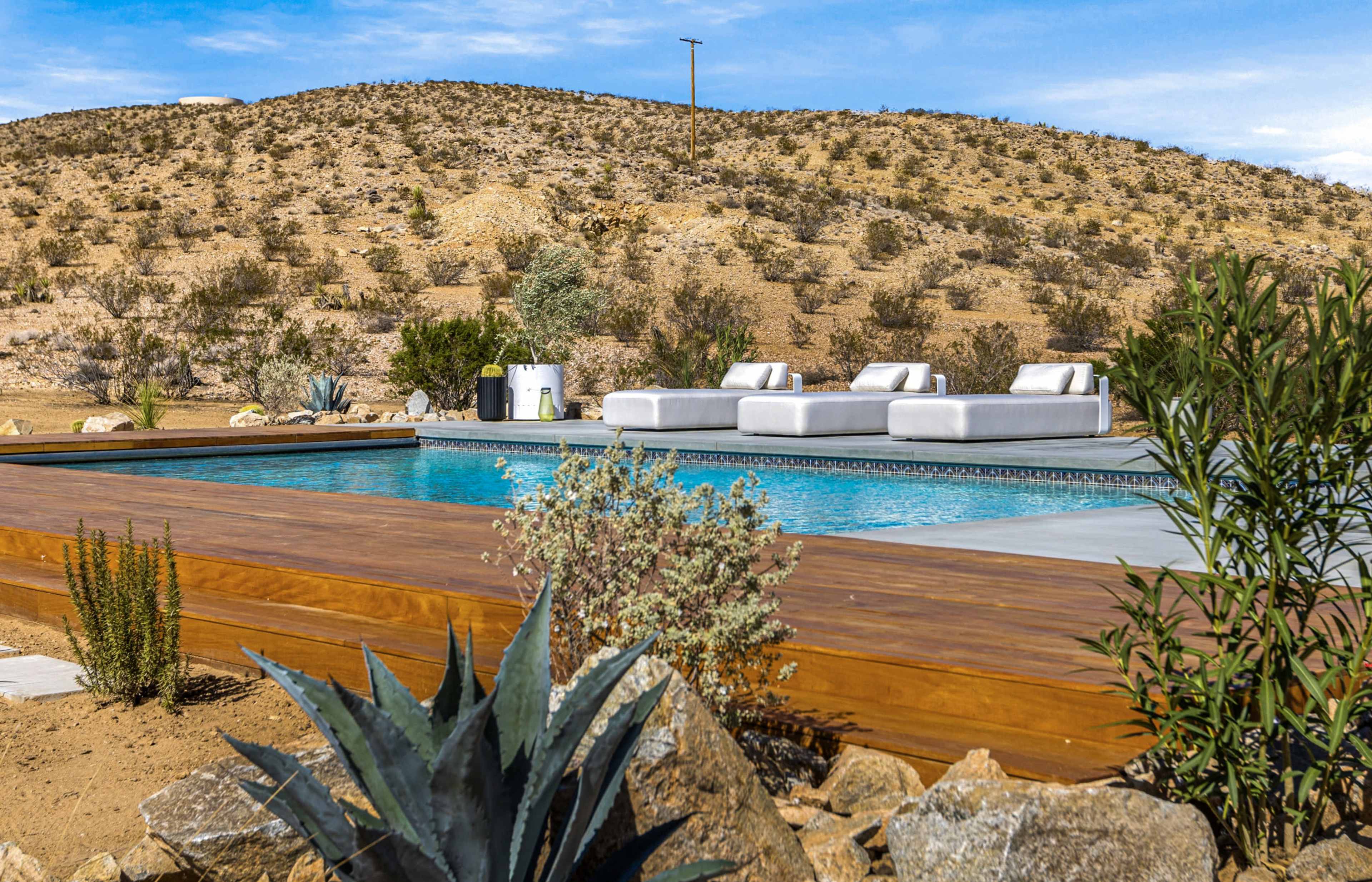 A modern swimming pool area surrounded by desert landscape, featuring lounge chairs and rocky terrain.