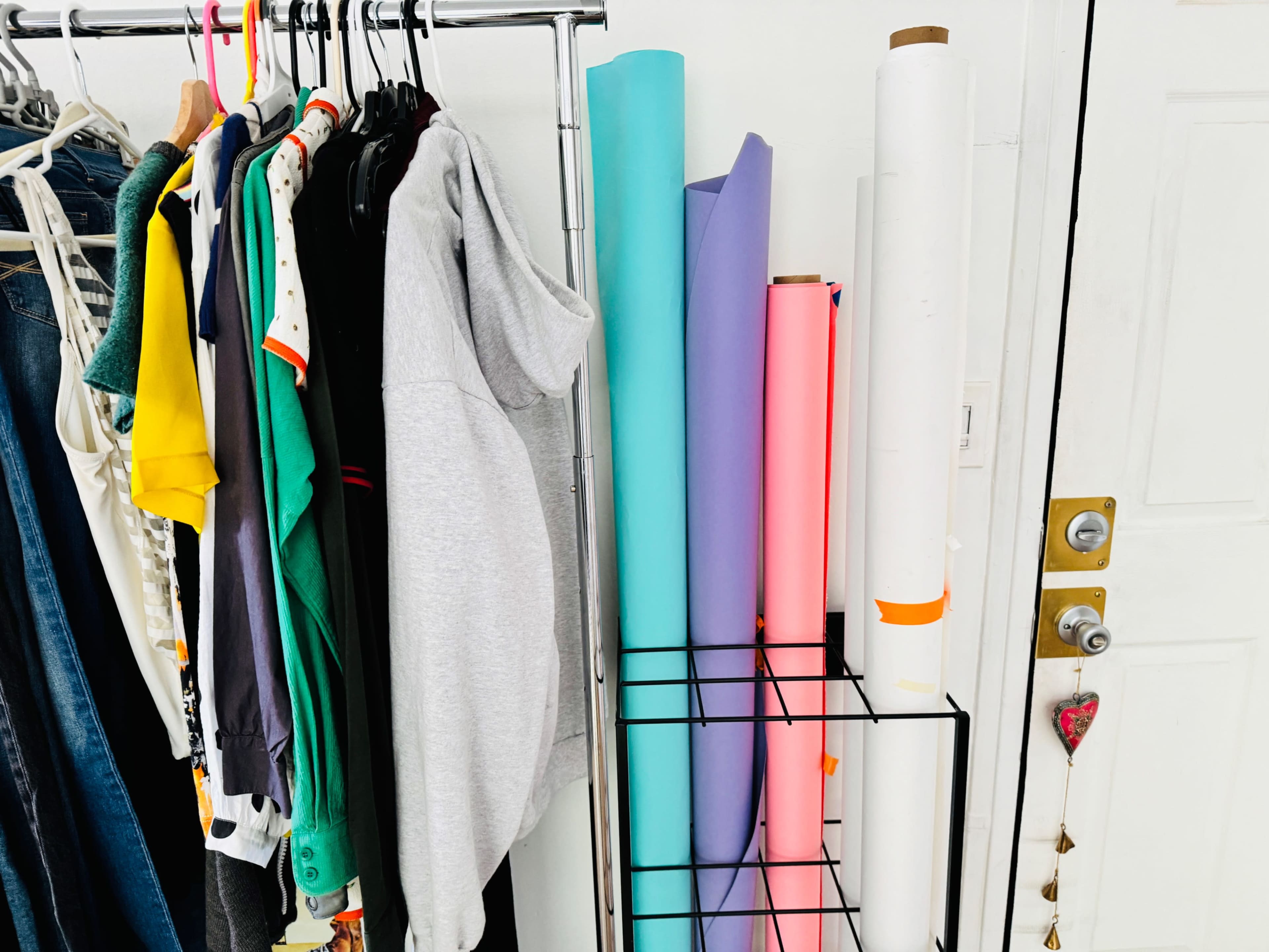A clothing rack with various garments hanging on one side and a stack of rolled papers in different colors on a metal stand beside it.