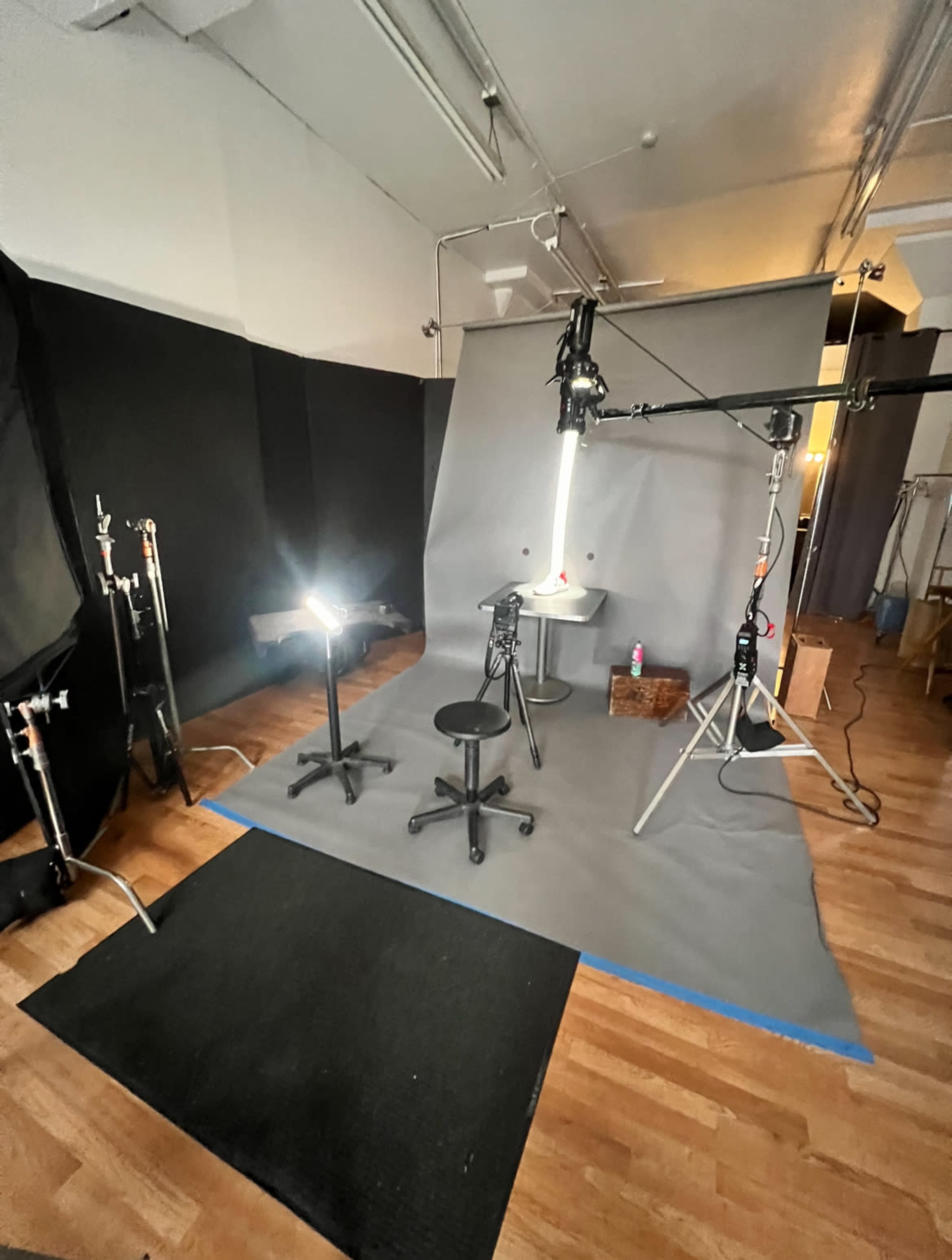 The image shows a photography studio set up with grey backdrops, lighting equipment, and chairs arranged around a central table.