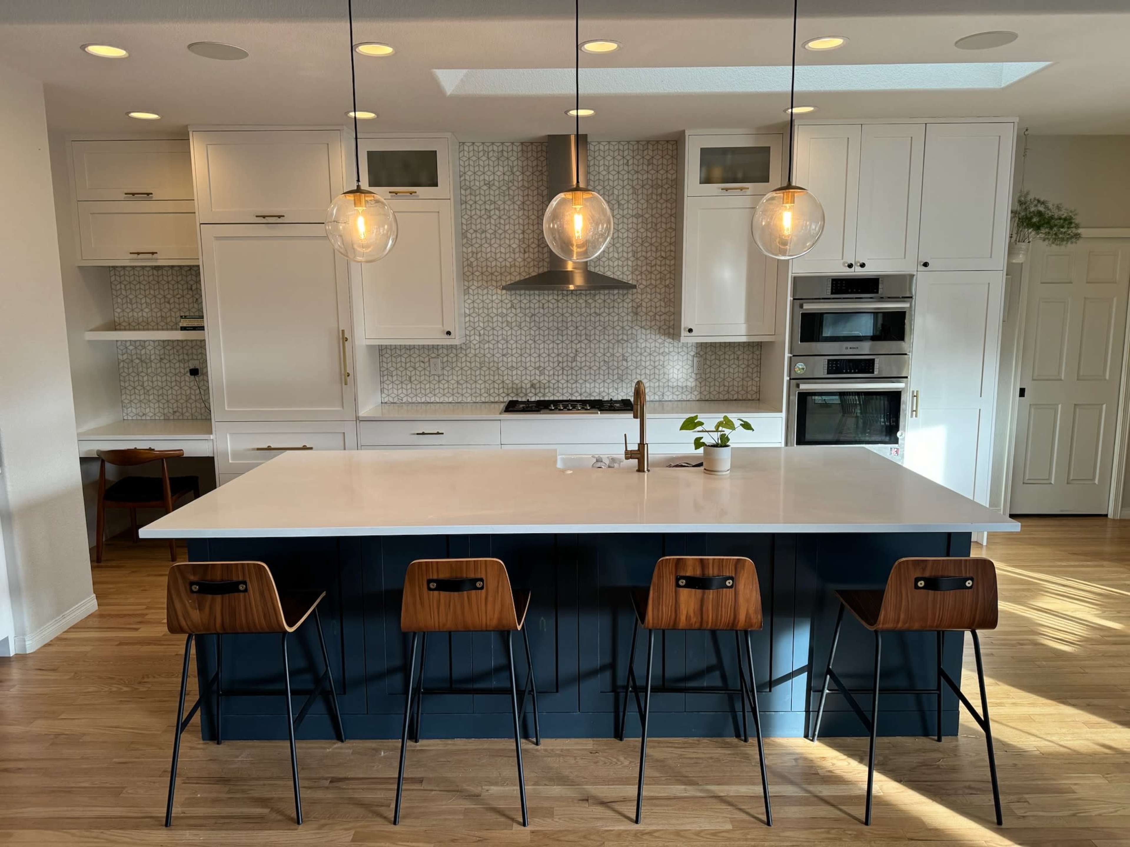 A modern kitchen featuring a large island with four bar stools, white cabinetry, and pendant lighting.