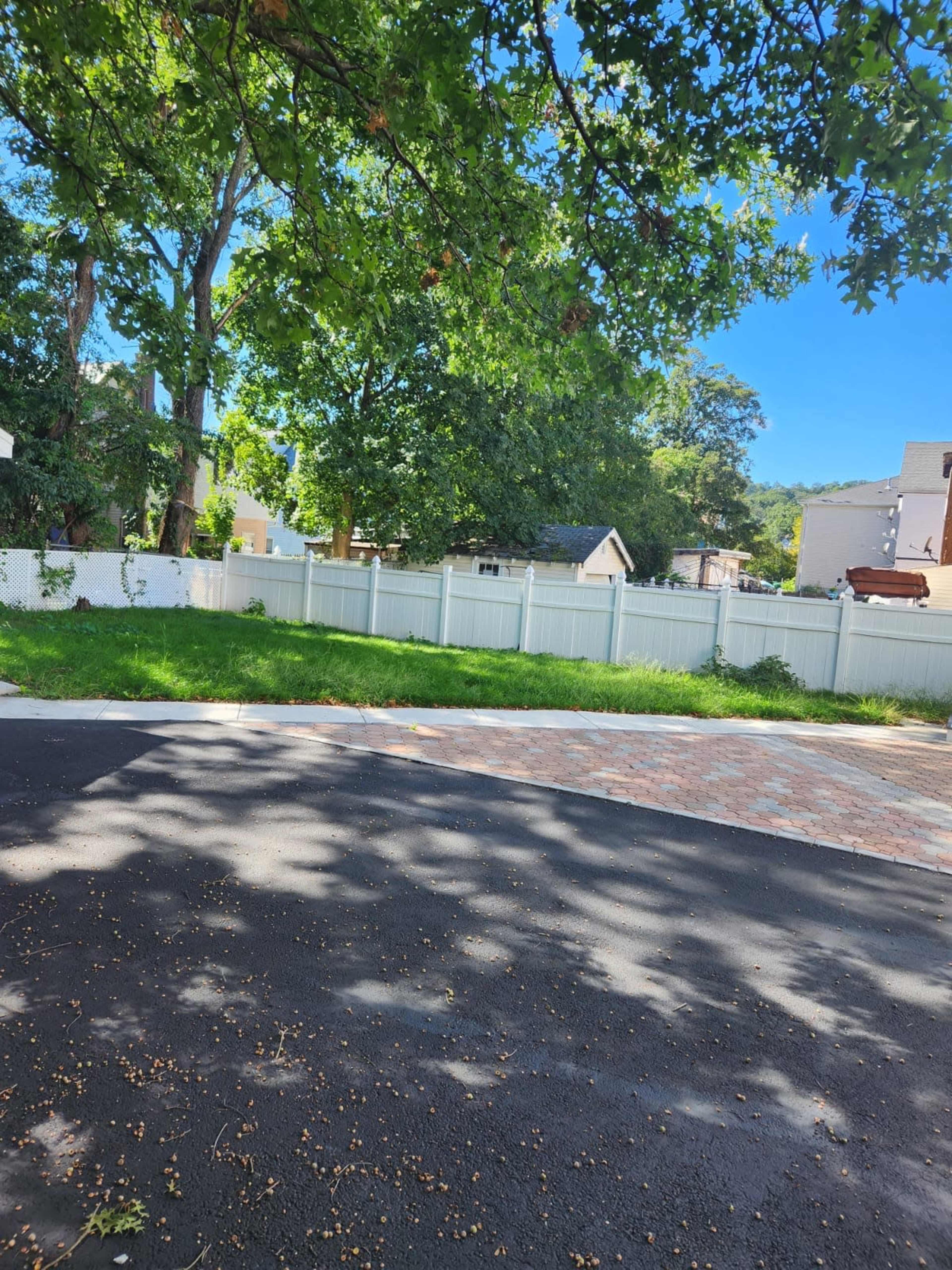 A green grassy area bordered by a white fence, with trees nearby and buildings in the background.
