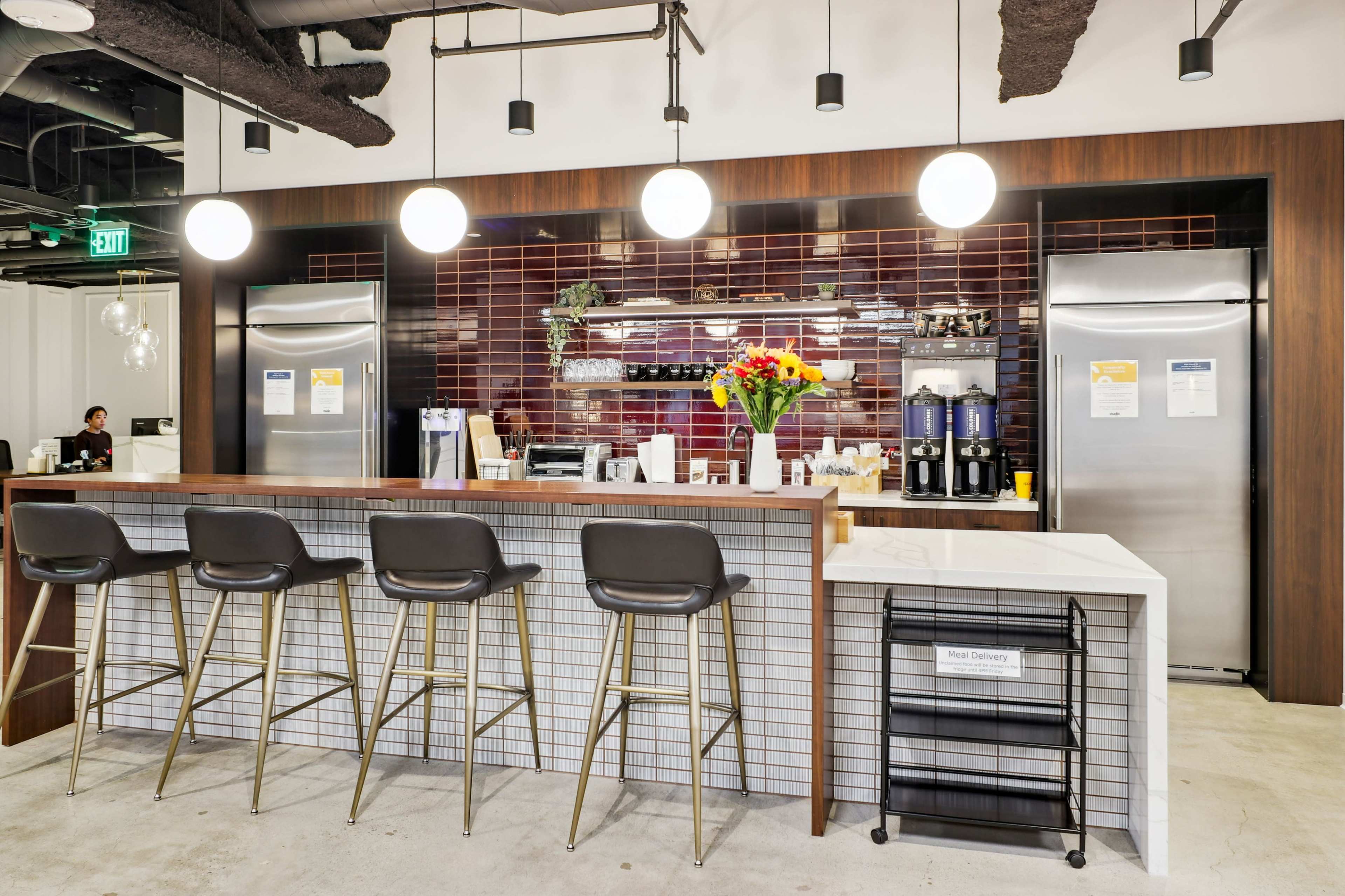 A modern kitchen area features a long bar with seating, stainless steel appliances, and decorative flowers on the counter.