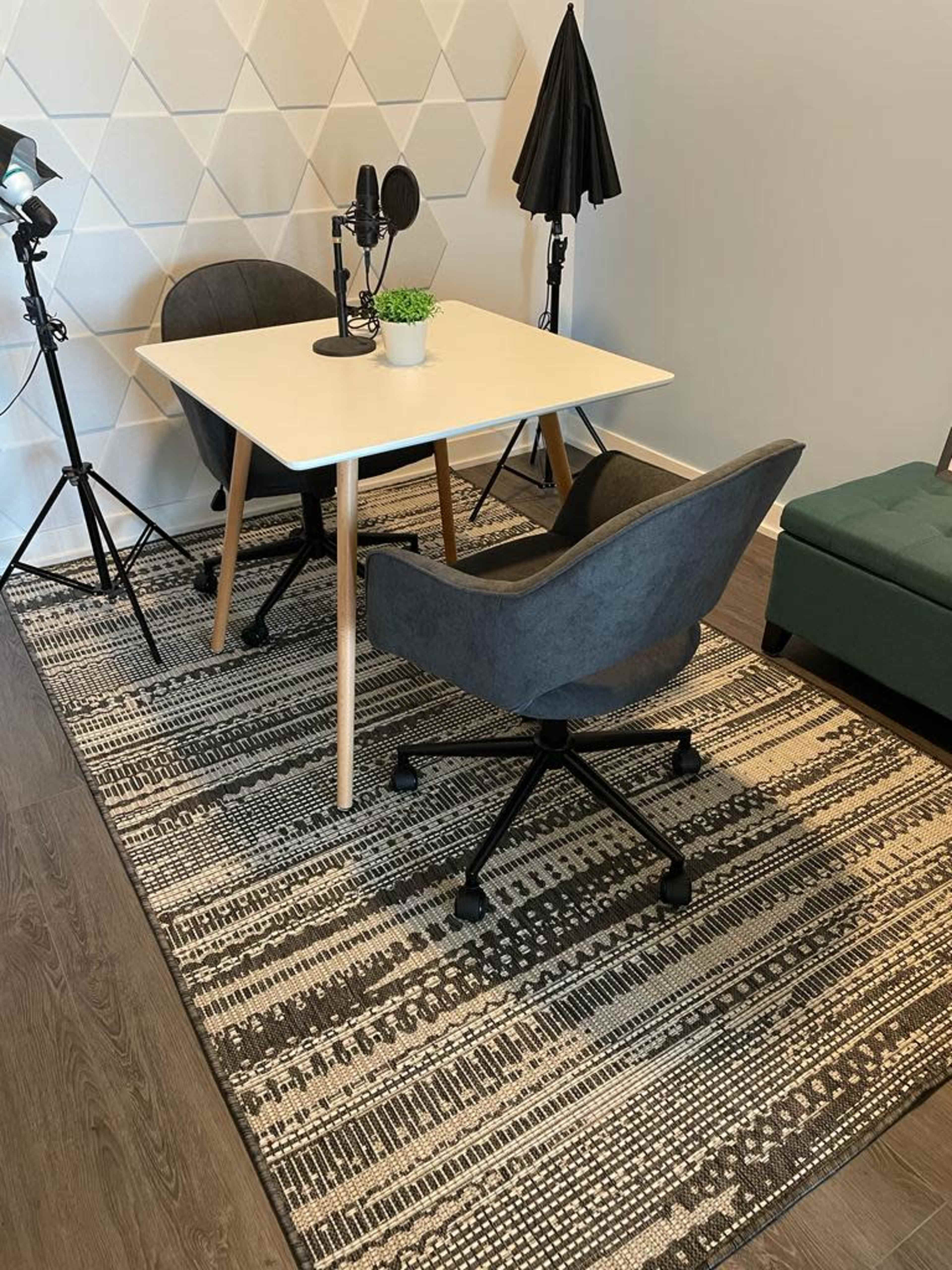 A small, modern workspace with a table, two chairs on a patterned rug, and photography equipment in the background.