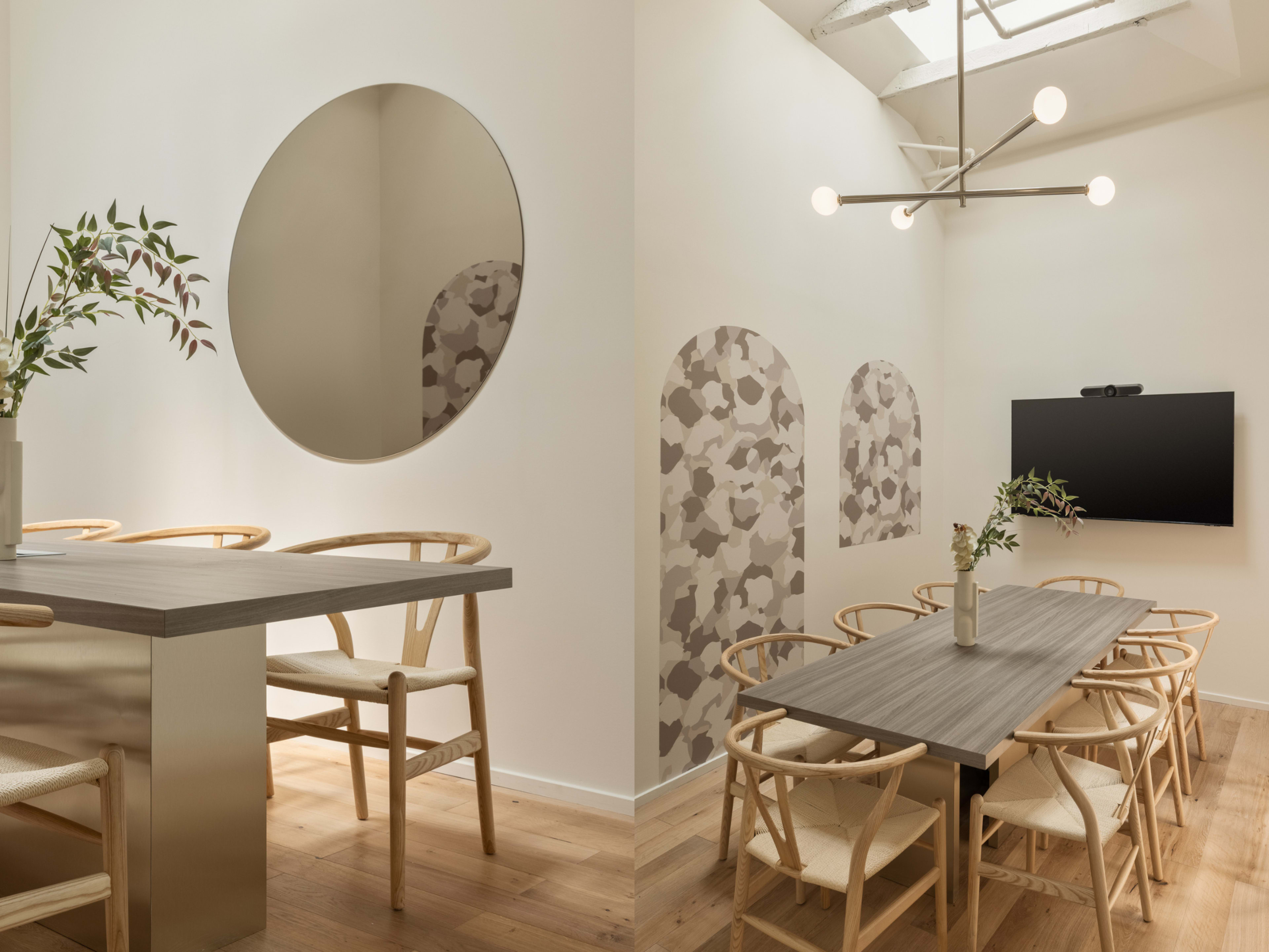 A modern dining area with a circular mirror, light wood floors, a large table surrounded by wooden chairs, and patterned wall decor.