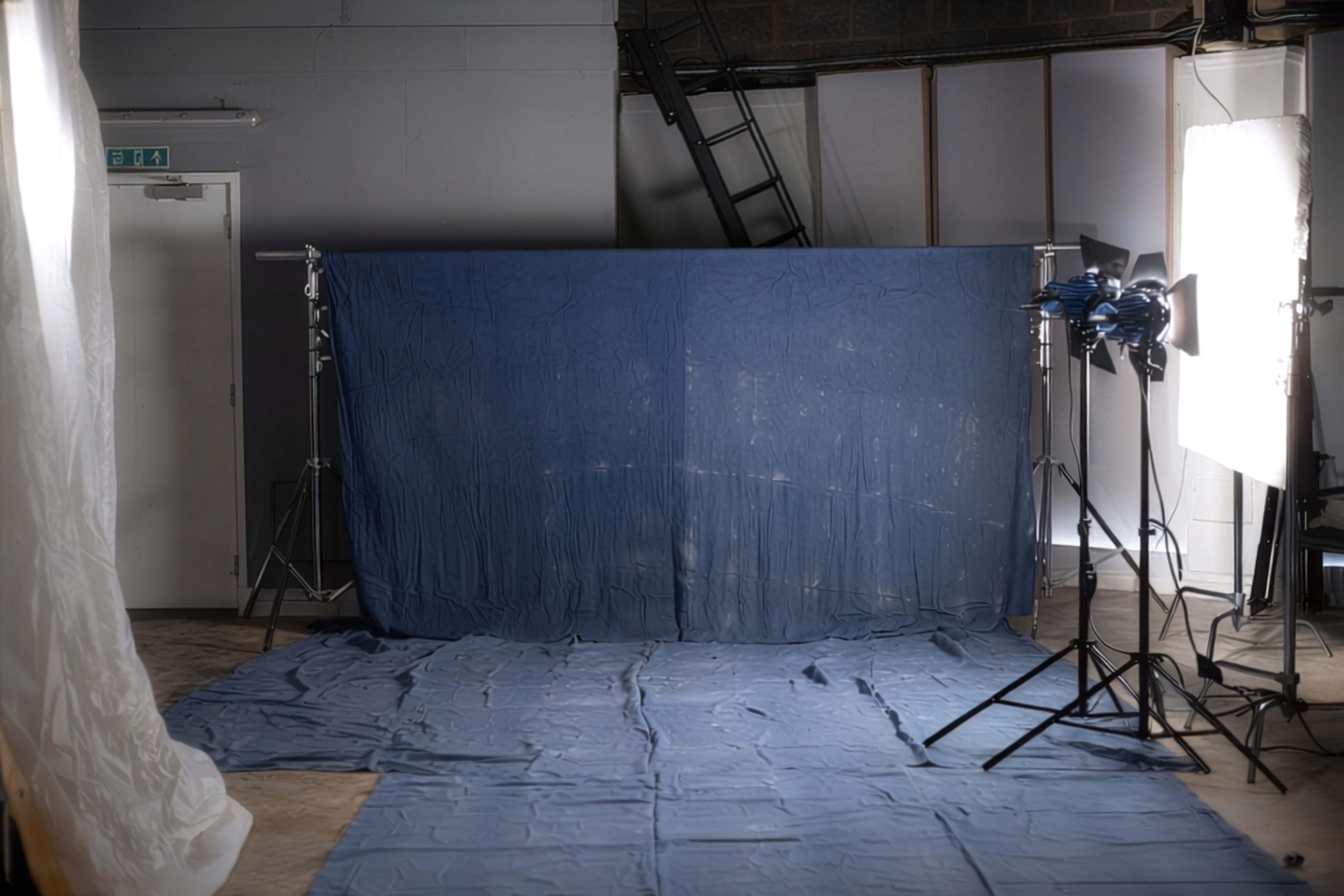 The image shows a photography studio setup with a blue backdrop, blue floor covering, and lighting equipment arranged on the right side.