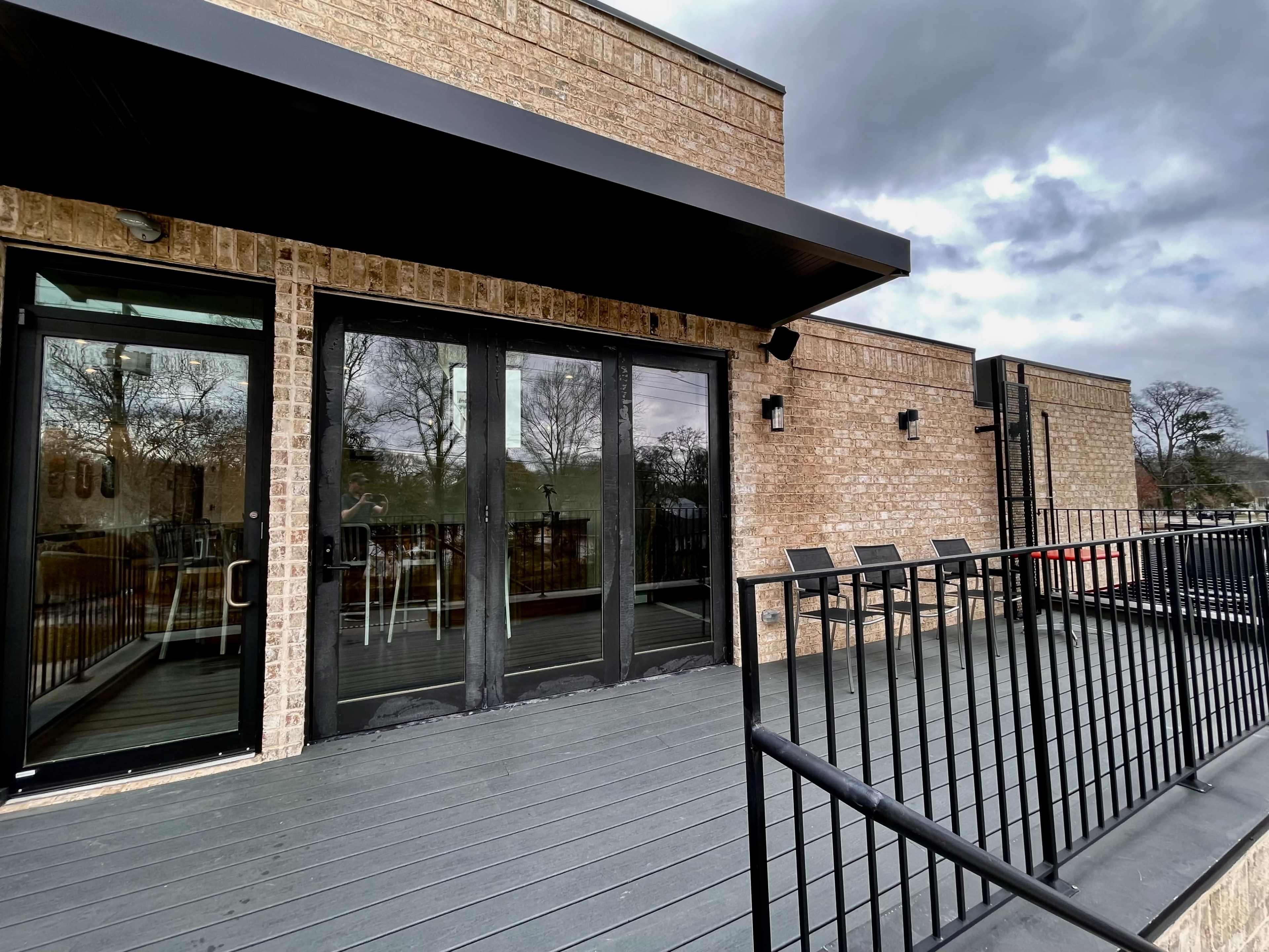 A modern building features a wooden deck with black railings and large glass doors.