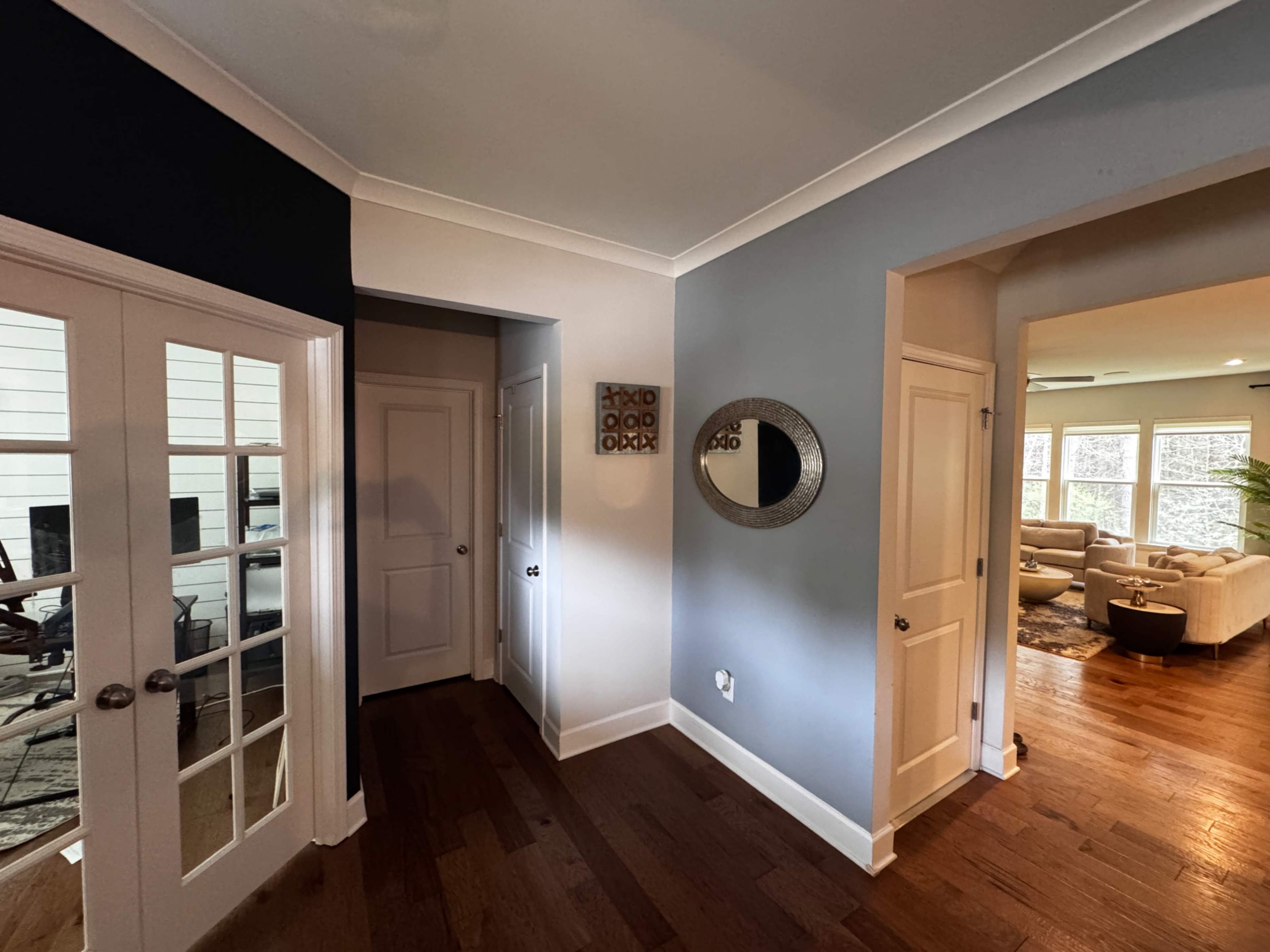 The image shows a hallway with a mirror on the wall, leading to a room visible on the right and a door on the left.