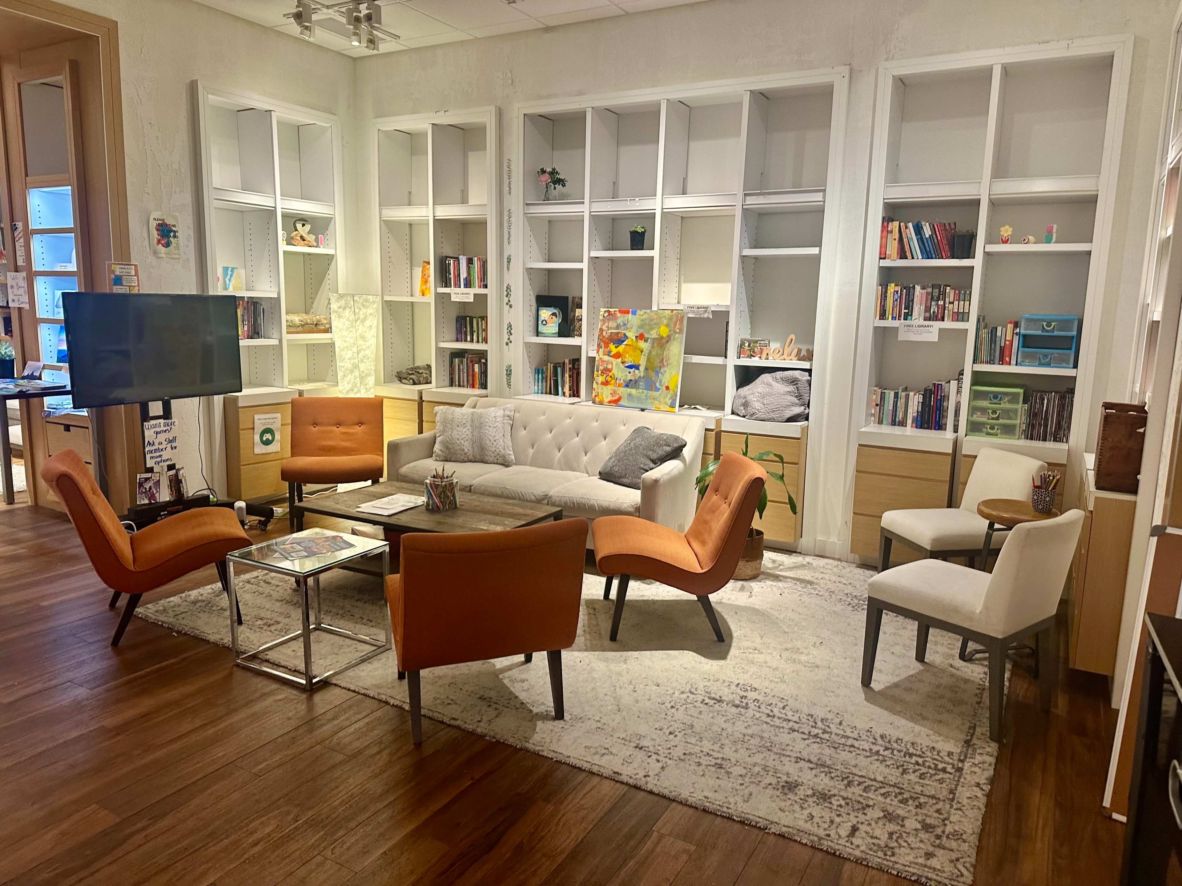 The image shows a modern living room with a sectional sofa, multiple armchairs, a coffee table, and built-in shelves filled with books and decorative items.