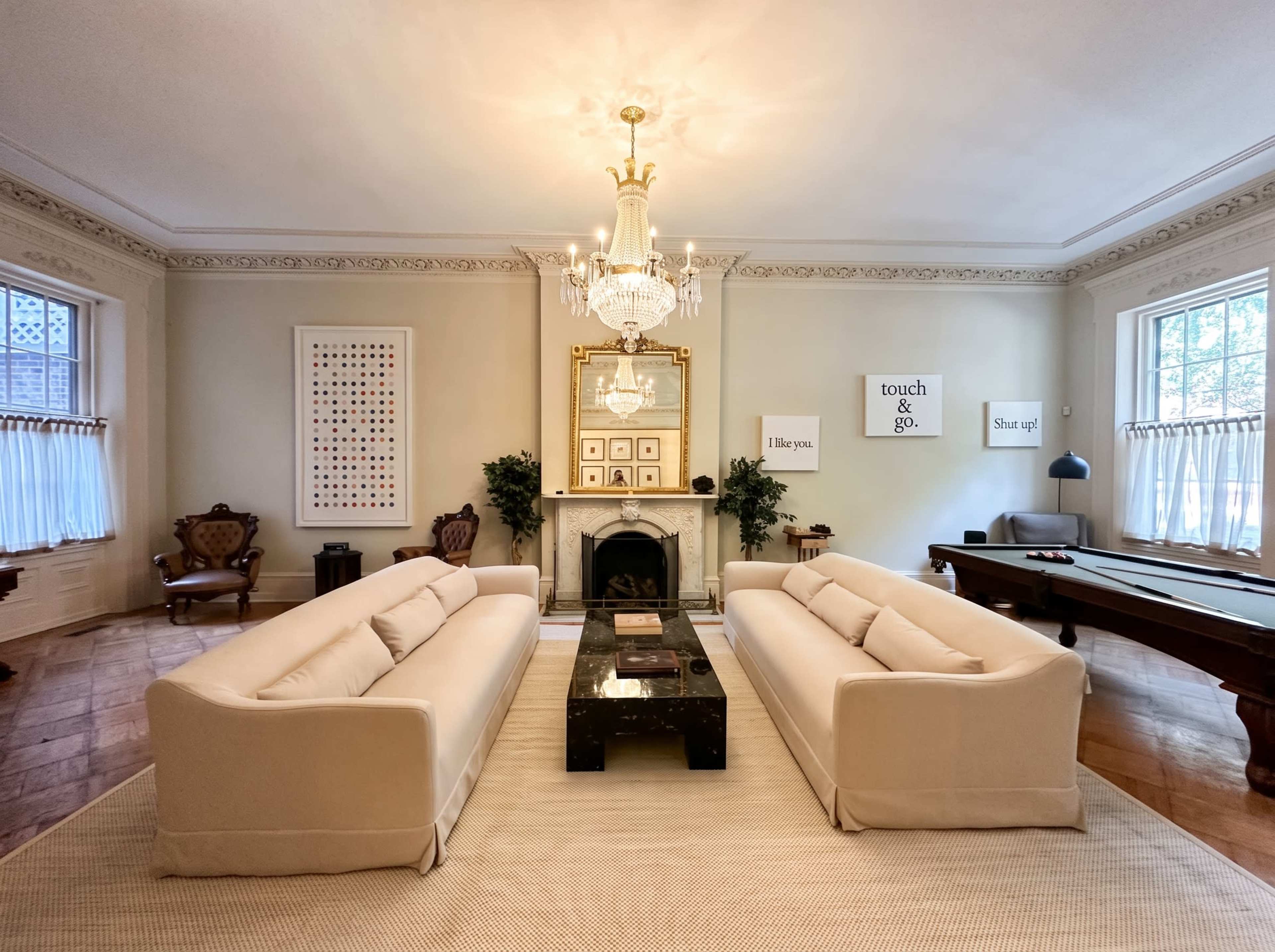 The image shows a stylish living room with two beige sofas facing a central black coffee table, a decorative fireplace, and a chandelier overhead.