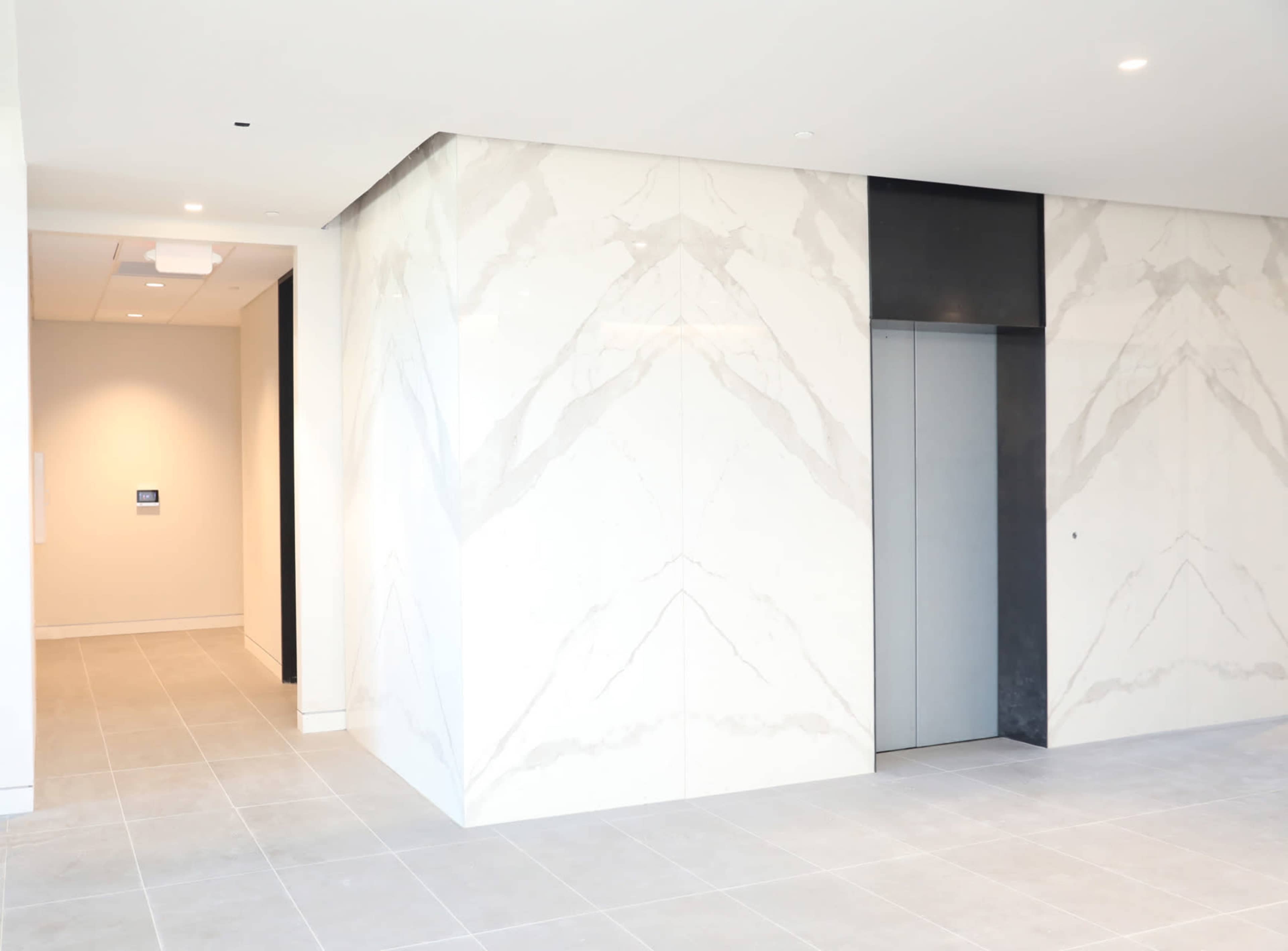 The image shows a modern lobby area with large marble walls and an elevator on the right side.