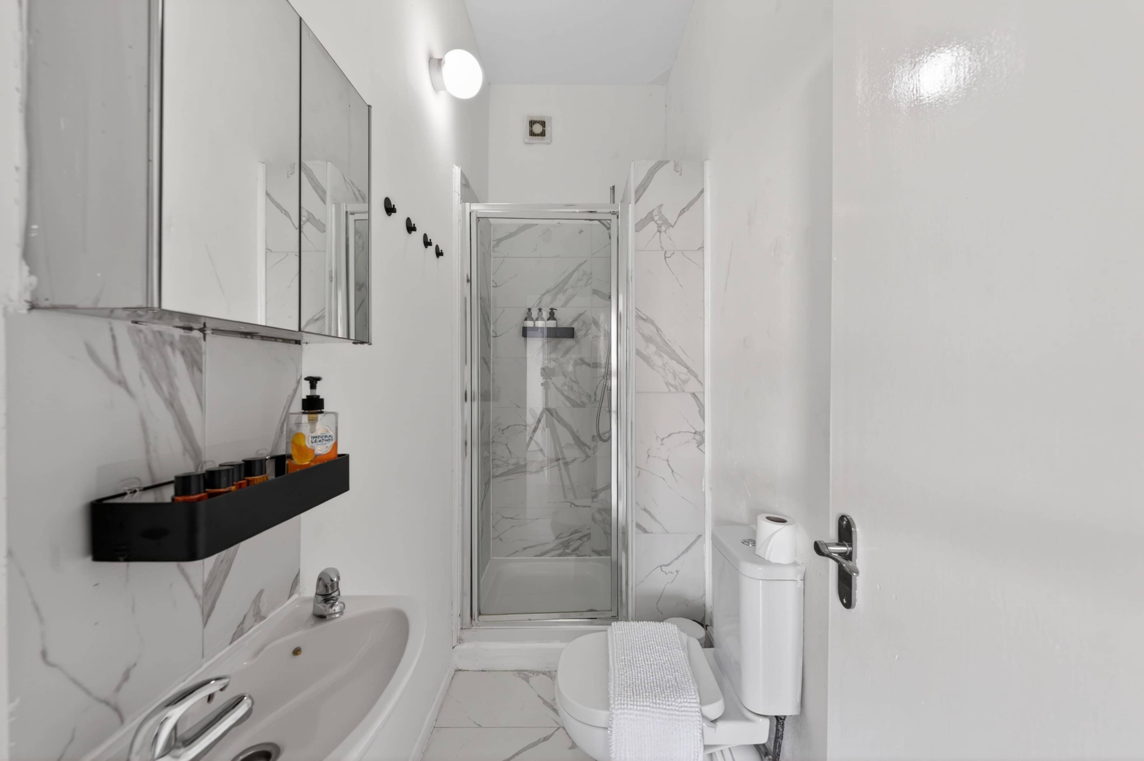 The image shows a modern bathroom featuring a shower cubicle with marble walls, a sink, a toilet, and a wall-mounted mirror.