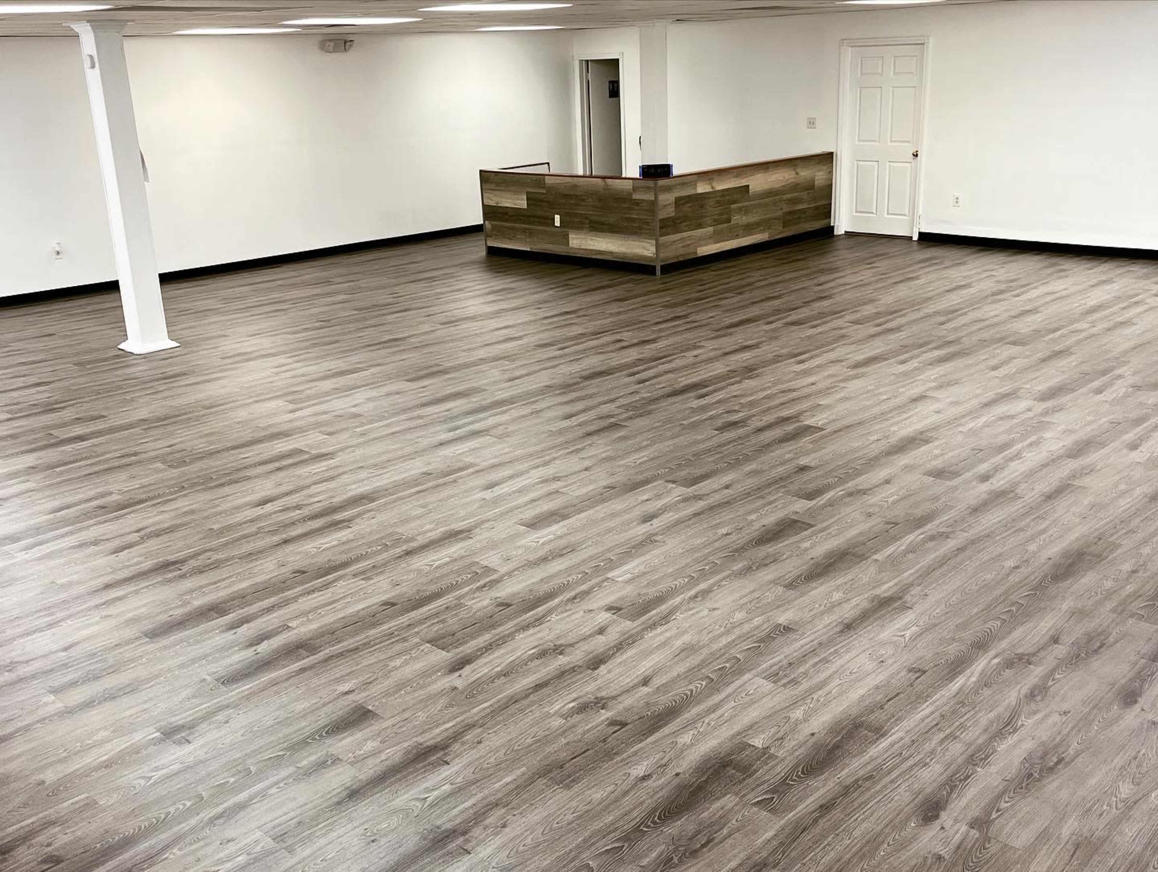 A spacious, empty room with a wooden reception desk in the background and a smooth wooden floor.