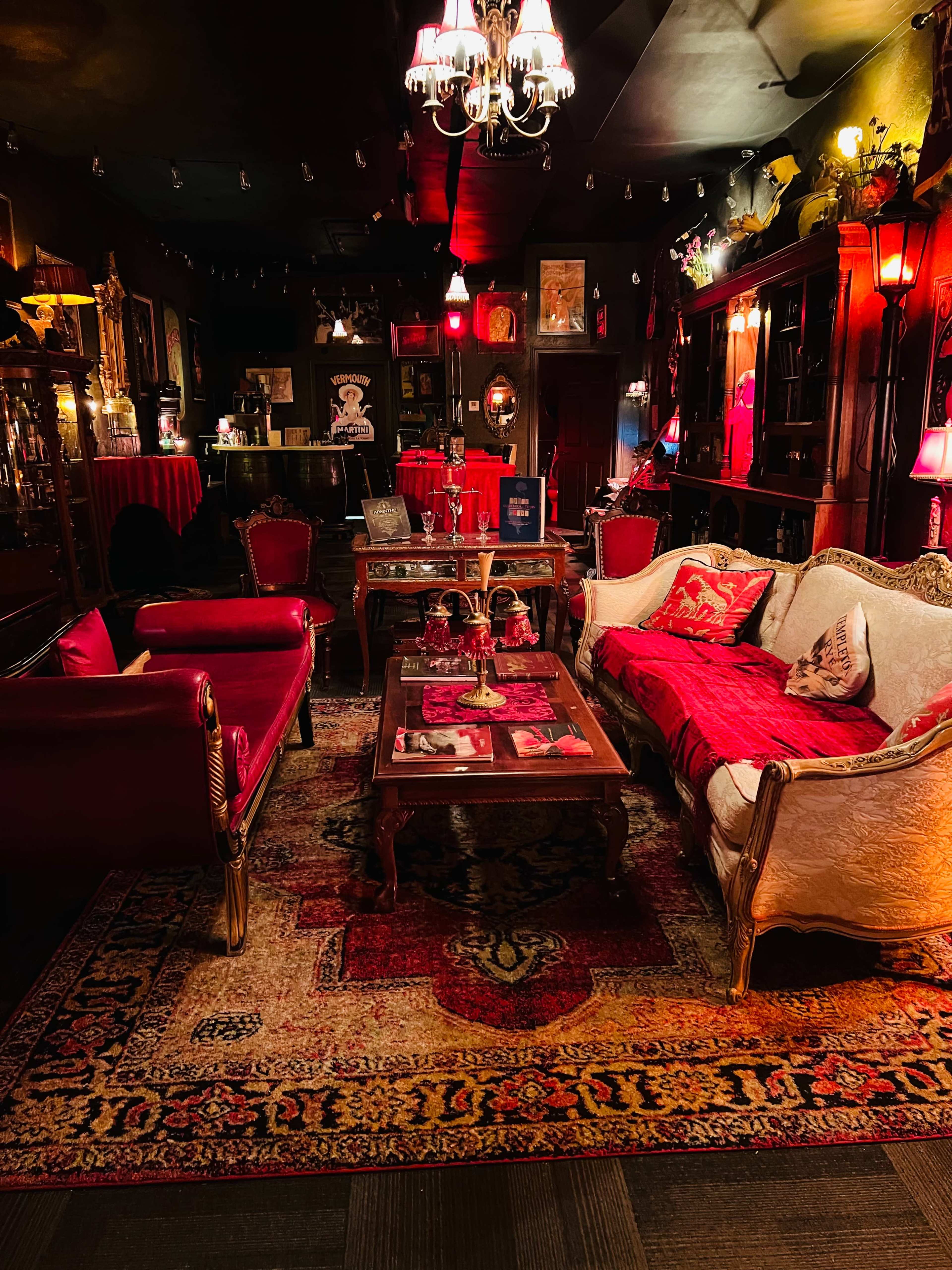 A dimly lit vintage-style parlor with ornate furnishings, red and gold accents, and a large, decorative rug.