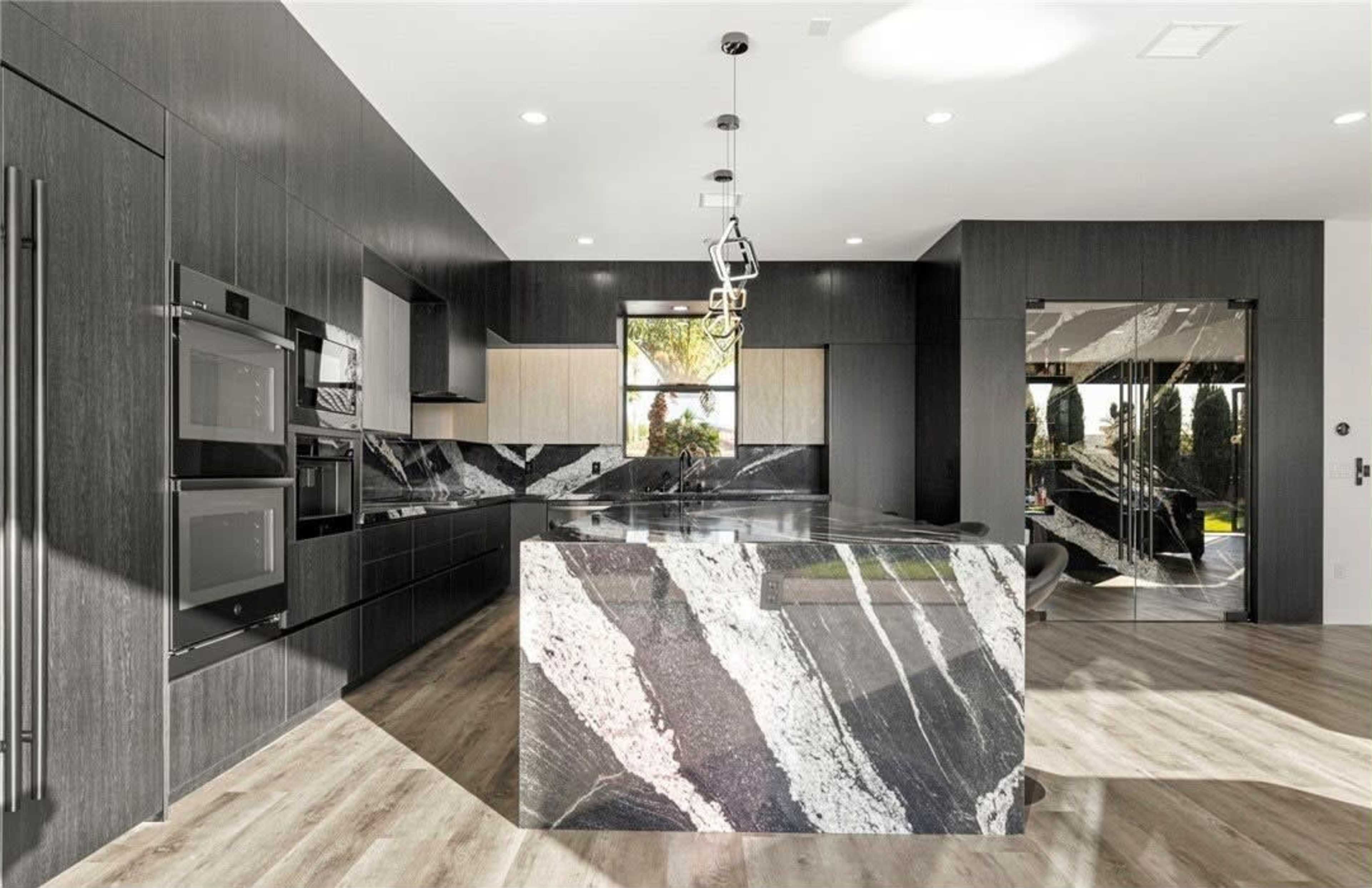 The image shows a modern kitchen featuring a black and white striped stone island, sleek cabinetry, and large windows that provide natural light.