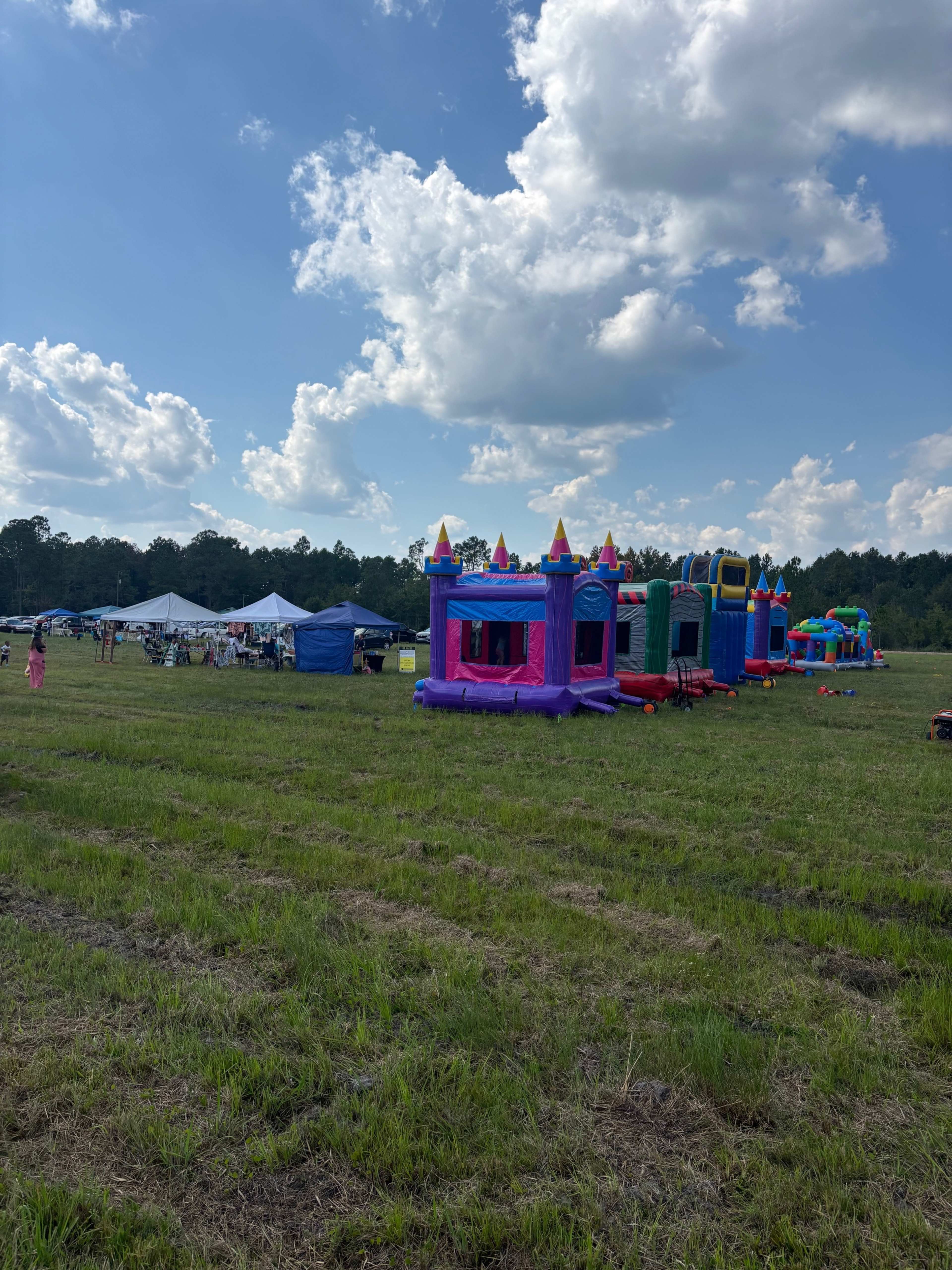 The image shows a field with several colorful inflatable bounce houses and tents set up for an outdoor event under a cloudy sky.