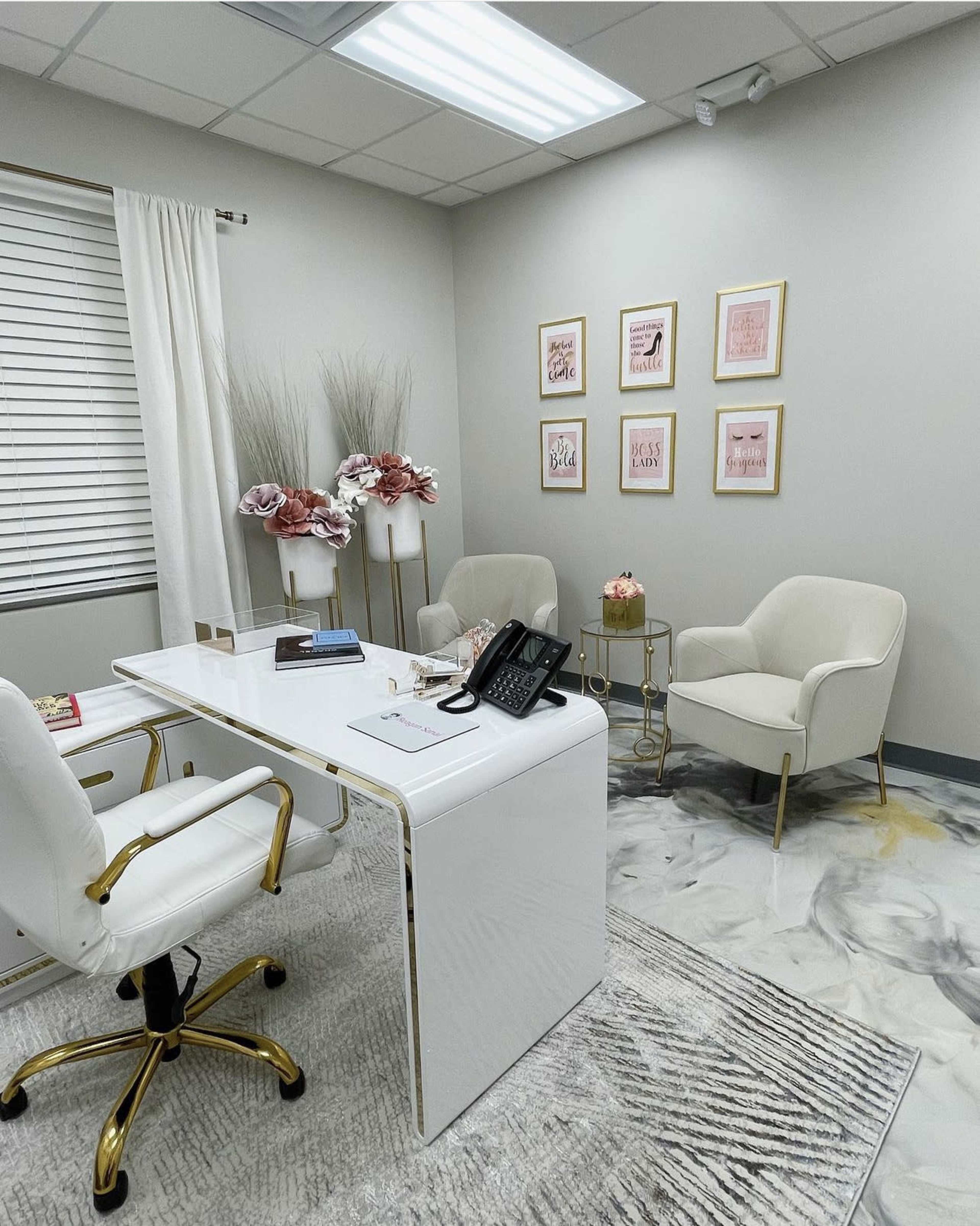 A modern office with a white desk, two chairs, a small round table, and framed artwork on the wall.