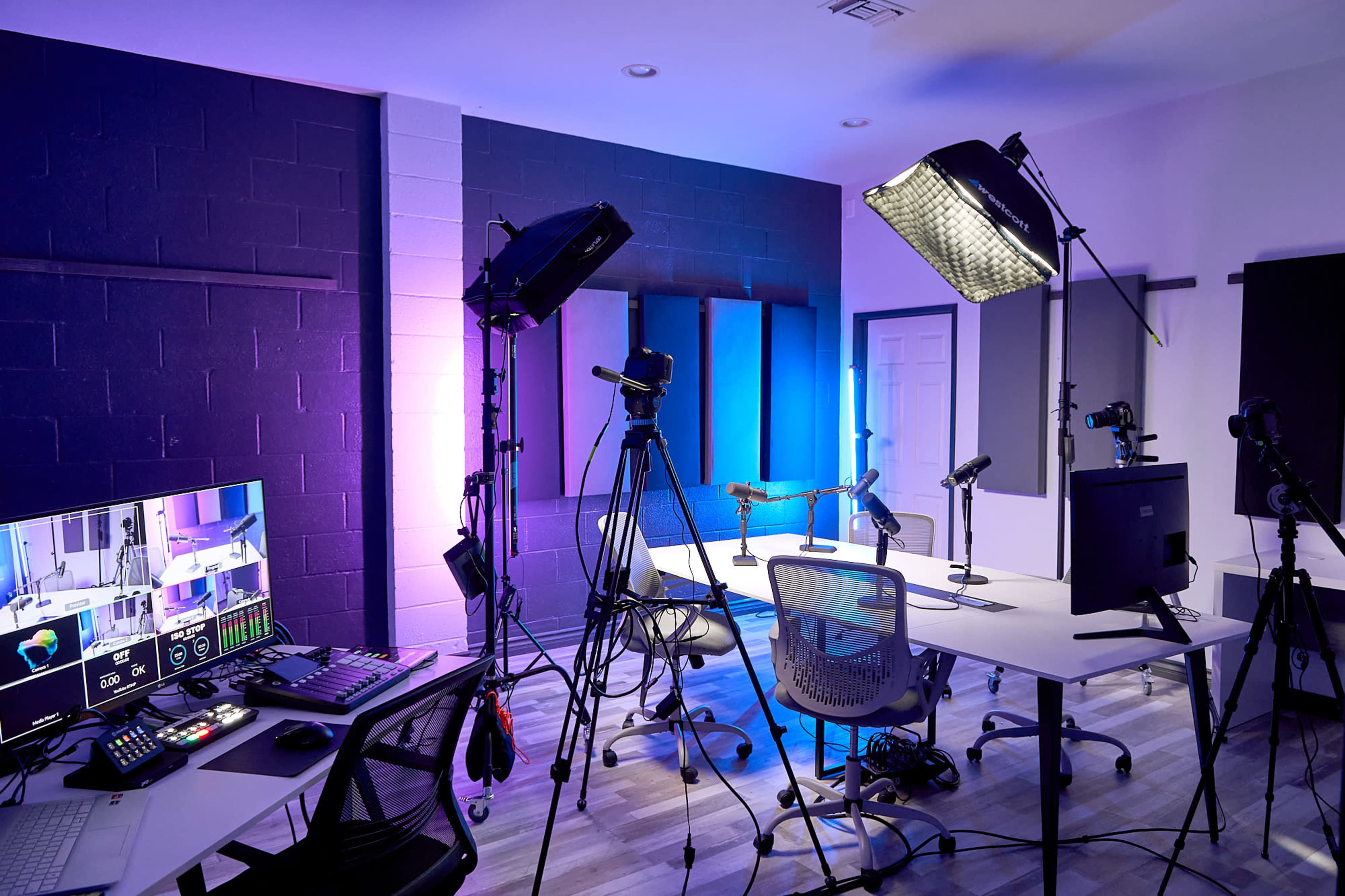 A modern studio set up with multiple cameras, lighting equipment, and a control panel arranged around a central table.