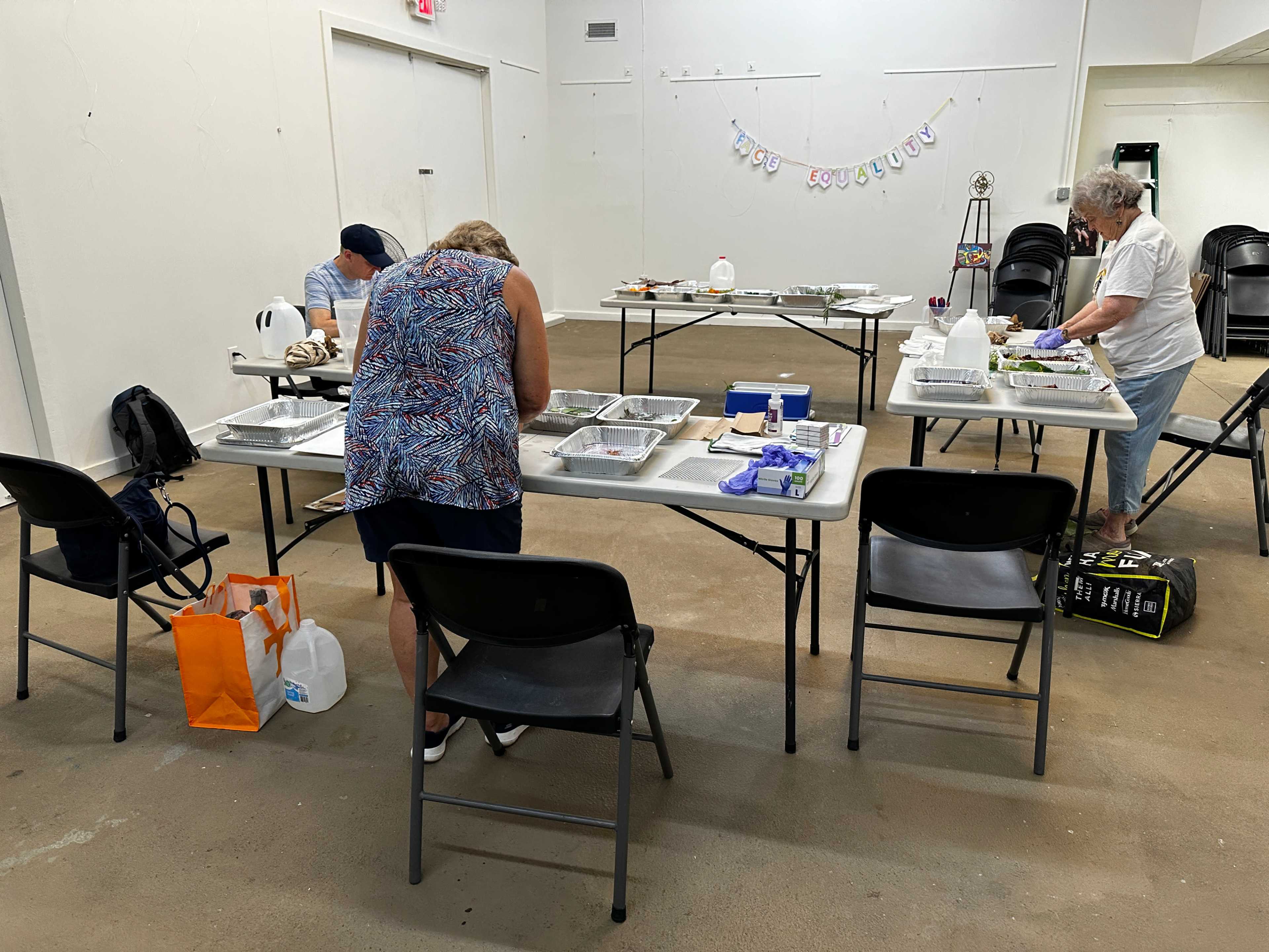 Several people are sitting at tables in a spacious room, working on crafts or projects with various supplies laid out before them.
