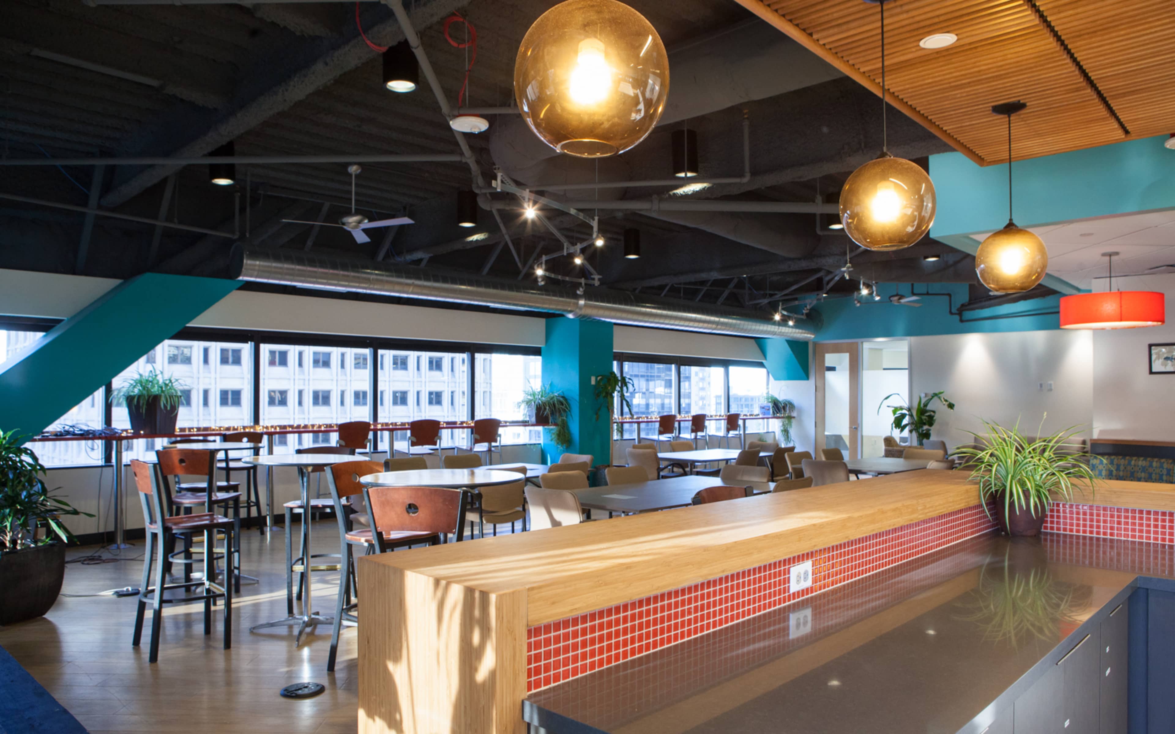 The image features a modern office space with a kitchenette, dining area, and large windows illuminated by pendant lights.