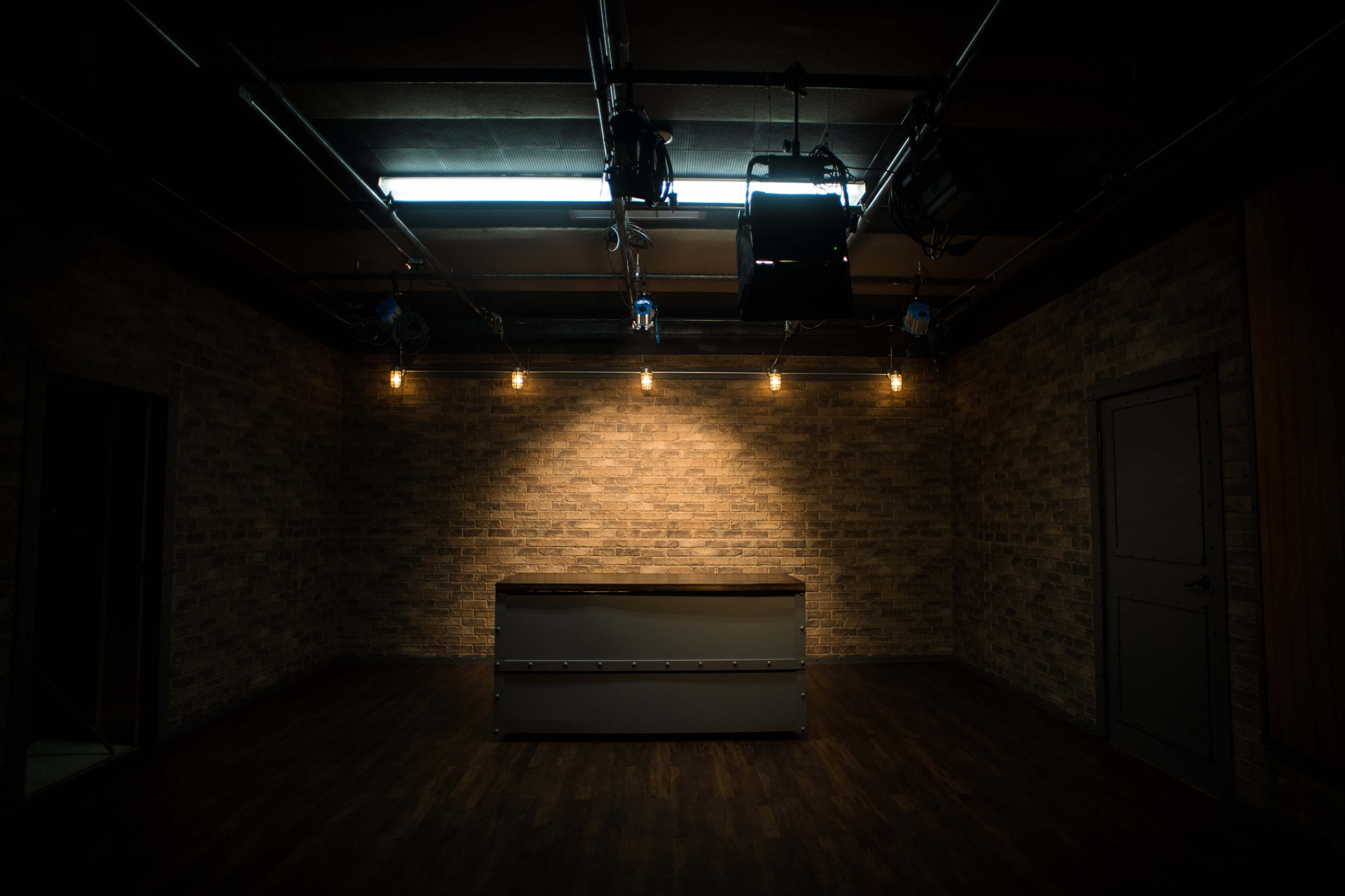 A dimly lit studio space with a central table, exposed brick walls, and overhead lighting.