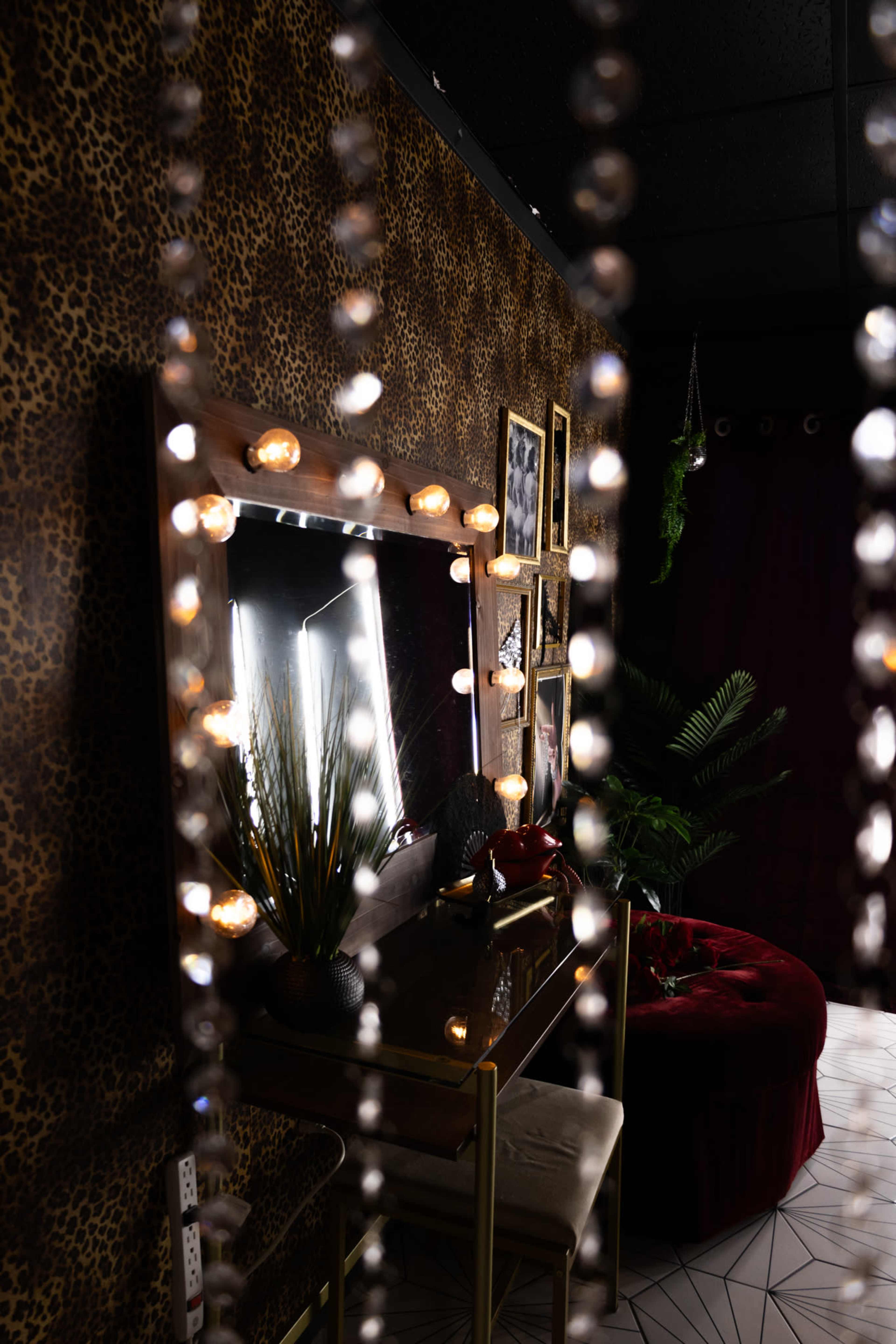 The image shows a stylish room featuring a mirror with decorative lights, a small table, and a plush red couch, all set against a leopard-print wallpaper backdrop.